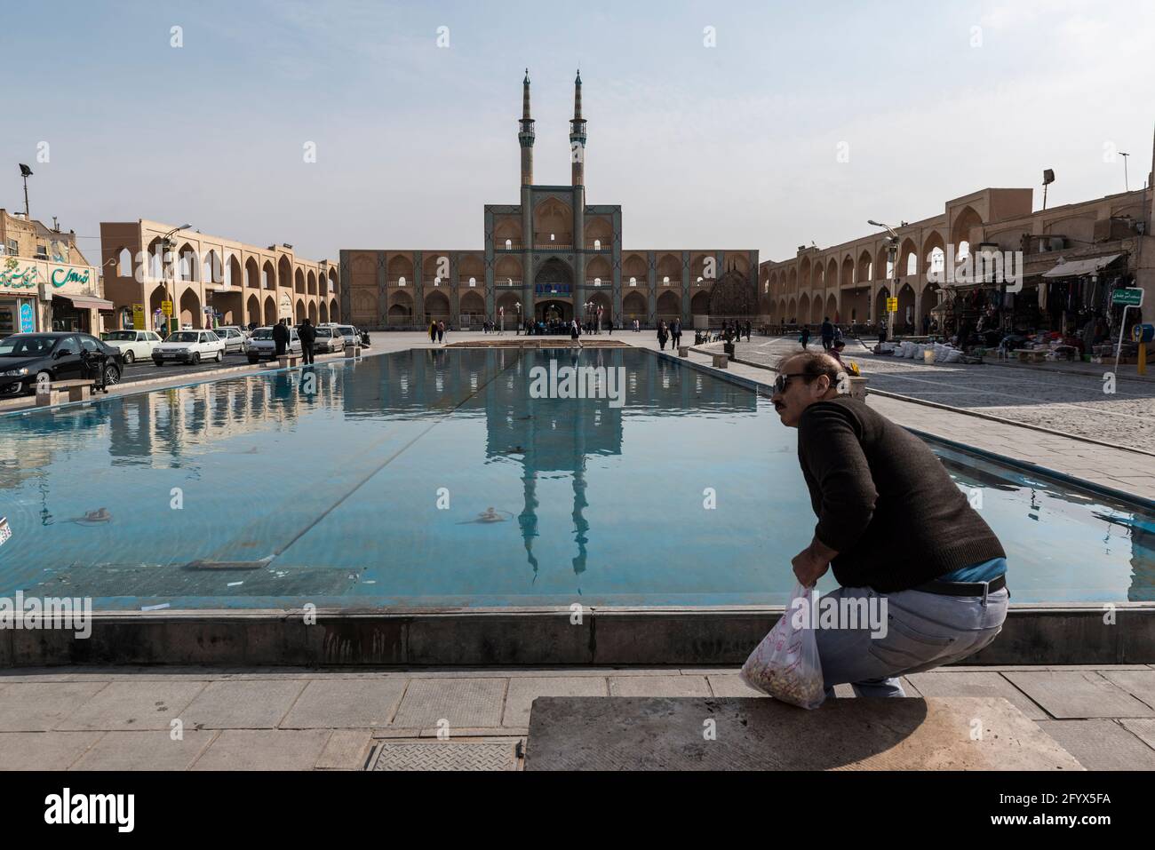 Männliche Person setzt sich auf eine Bank mit Blick auf den großen Pool und die Moschee auf dem Amir Chakhmaq Platz. Yazd, Provinz Yazd, Iran. Stockfoto