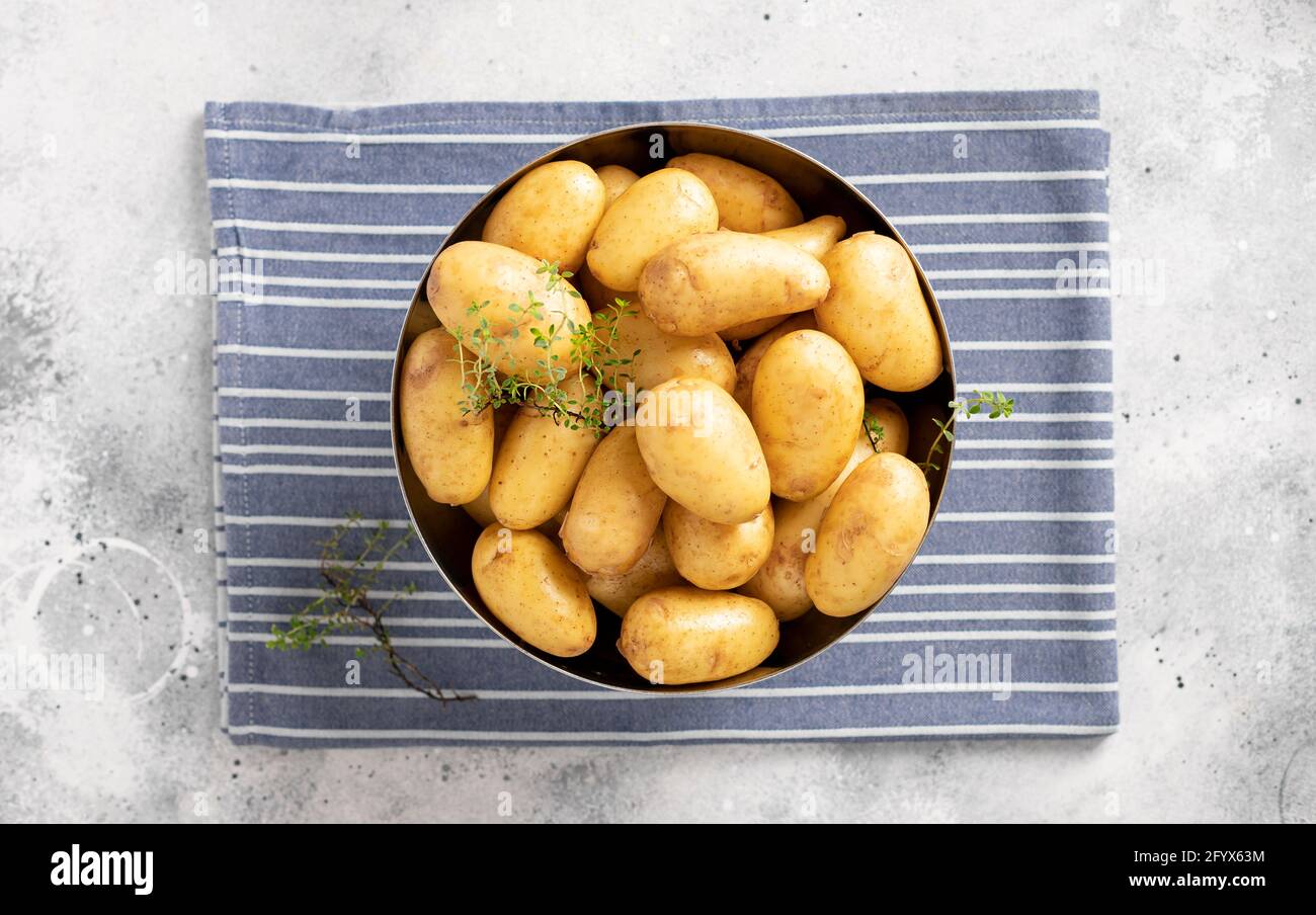 Rohe Kartoffeln in Metallschüssel auf blauem Küchentuch. Gemüsefutter. Draufsicht. Grauer Hintergrund. Horizontales Bild. Stockfoto