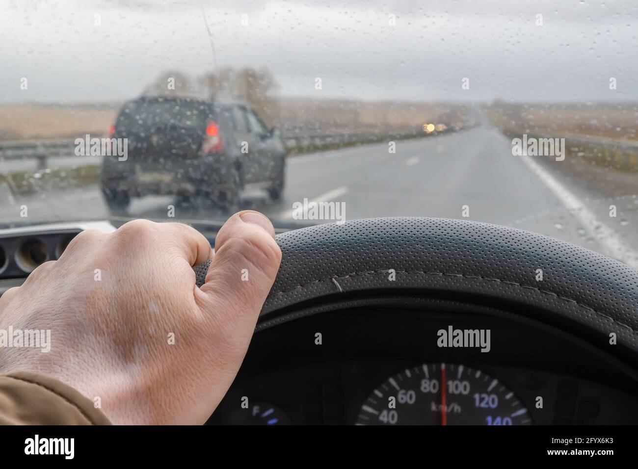 Fahrerhand am Lenkrad im Fahrzeug und Regentropfen an der Windschutzscheibe Stockfoto