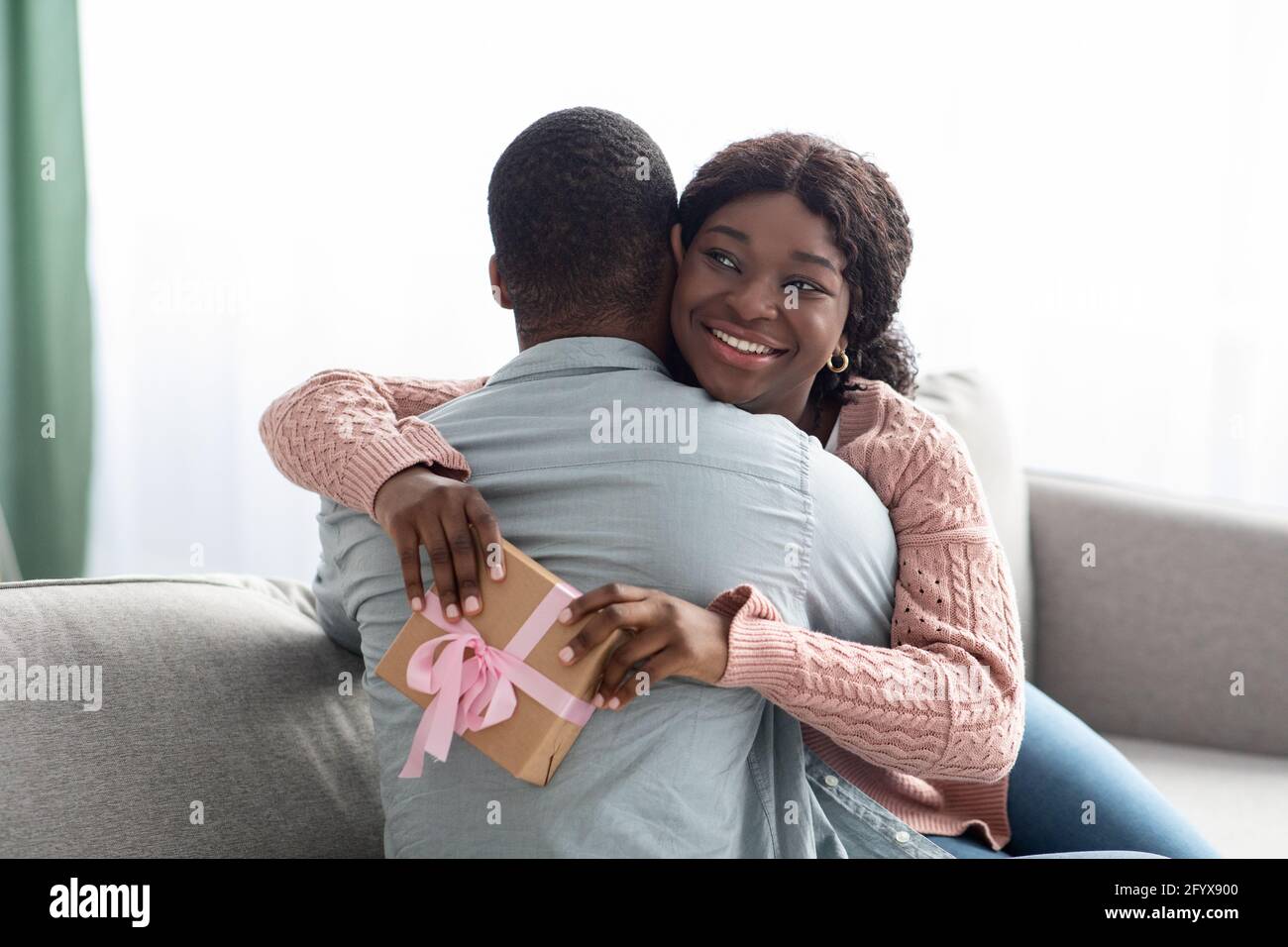 Emotionale afroamerikanische Dame mit Geschenk umarmt ihren Geliebten Stockfoto Emotionale afroamerikanische Dame mit Geschenk umarmt ihren Geliebten Stockfoto