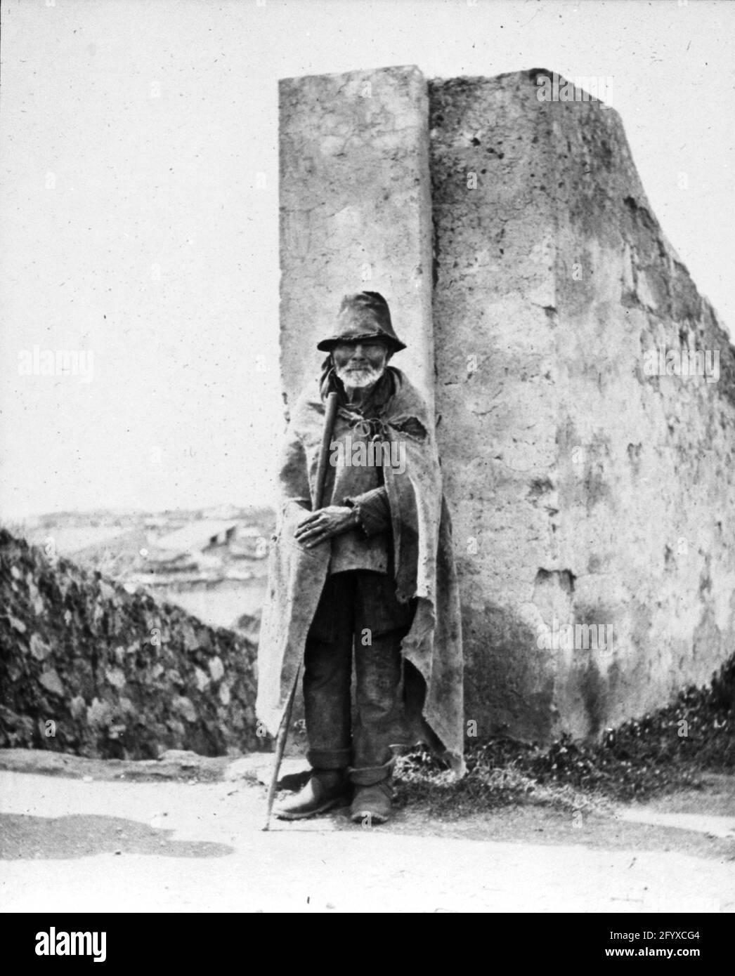 Ein älterer Mann mit einem Stock steht neben einer alten Mauer, Pompeji, Italien, 1890. (Foto von Burton Holmes) Stockfoto