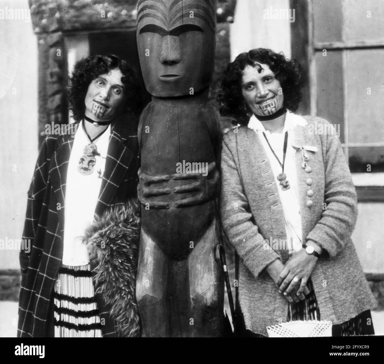 Maori-Zwillinge stehen auf beiden Seiten einer traditionellen Holzstatue, Rotorua, Neuseeland, 1917. (Foto von Burton Holmes) Stockfoto