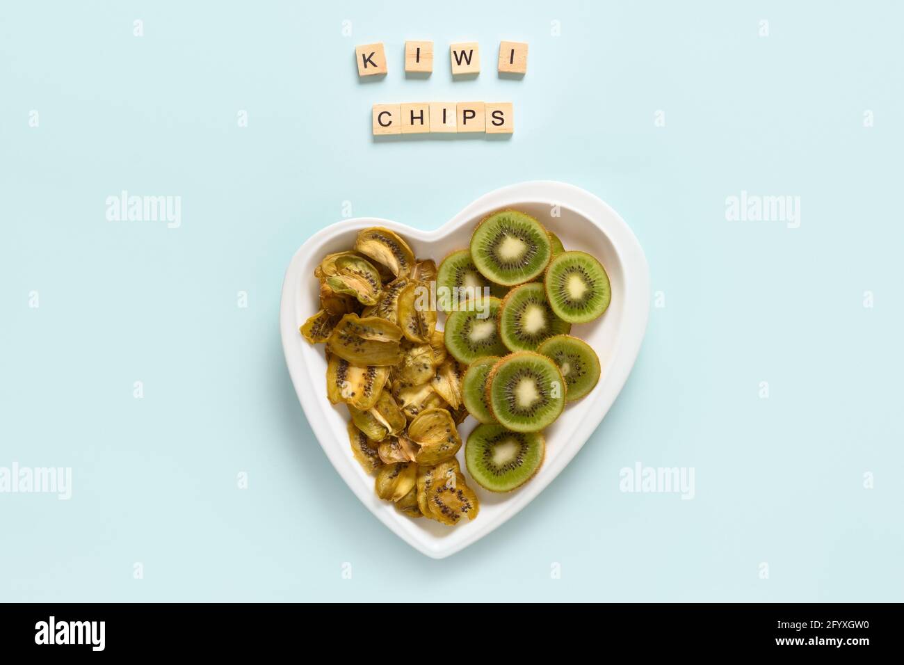 In Scheiben geschnittene frische und getrocknete Früchte Kiwi-Chips in Form eines Herztellers auf blauem Hintergrund. Veganes und zuckerfreies Dessert für Kinder. Blick von oben. Heimtrocknung Stockfoto