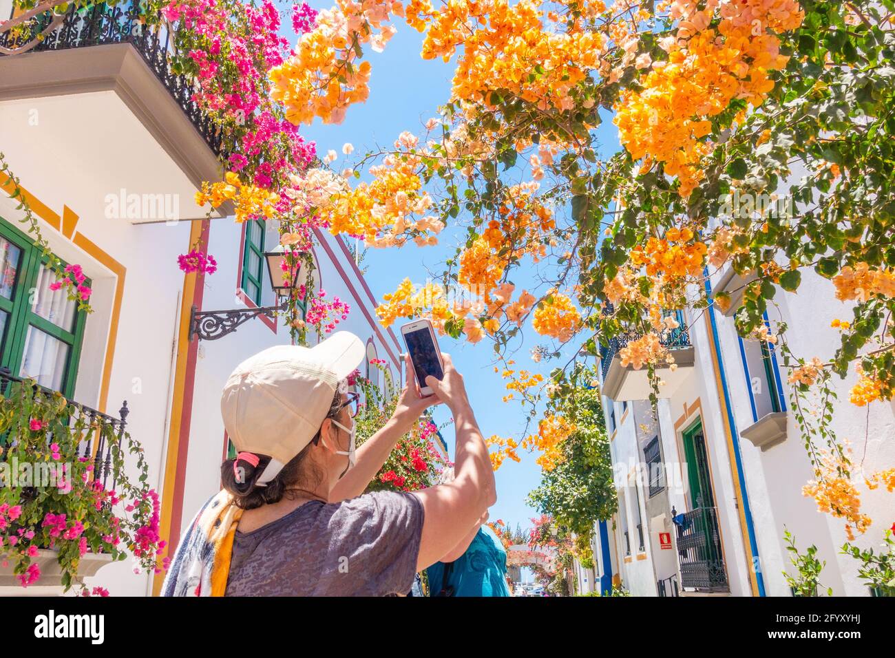 Touristen, die Covid-Gesichtsmasken tragen und Fotos von Bougainvillea in Puerto de Mogan, Gran Canaria, Kanarische Inseln, Stockfoto