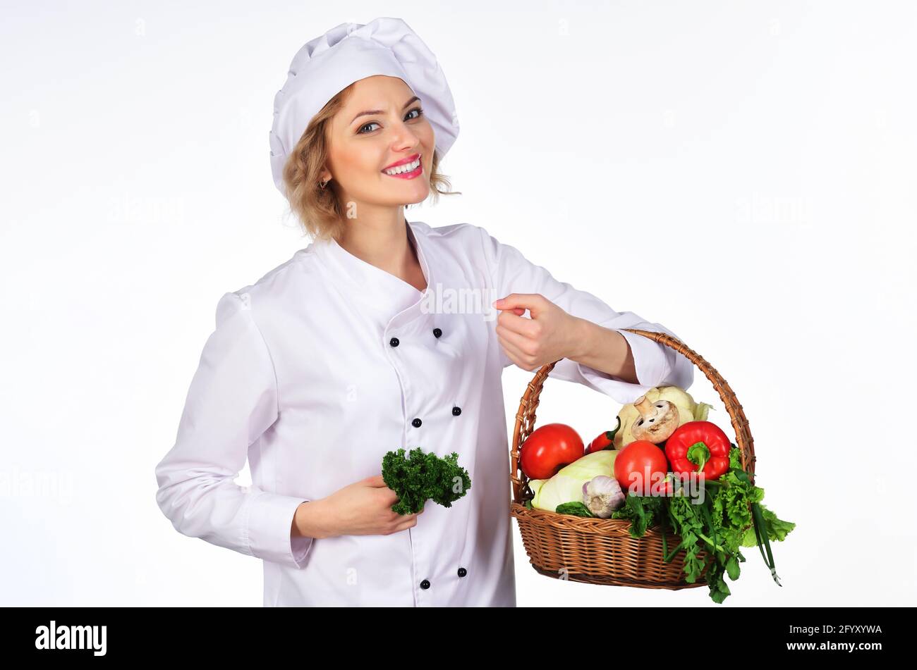 Lächelnde Küchenchefin mit Gemüsekorb. Professioneller Koch mit Korb mit frischem Gemüse. Bio-Food-Konzept. Stockfoto