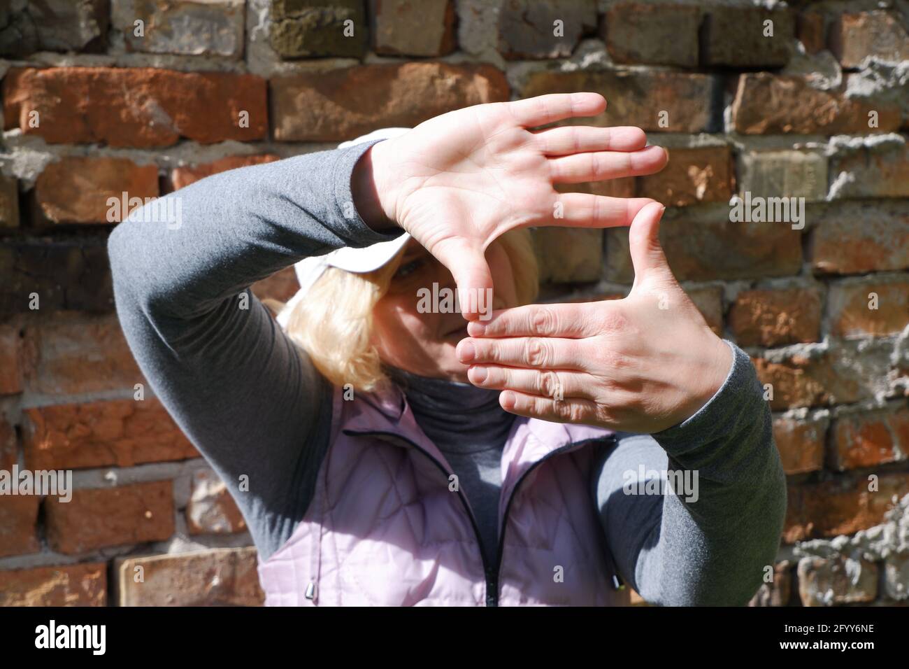 Ein Mädchen in der Nähe einer Mauer mit ihren Händen stellt sich eine Kamera vor. St. Veronica's Day Photographer's Day . Stockfoto