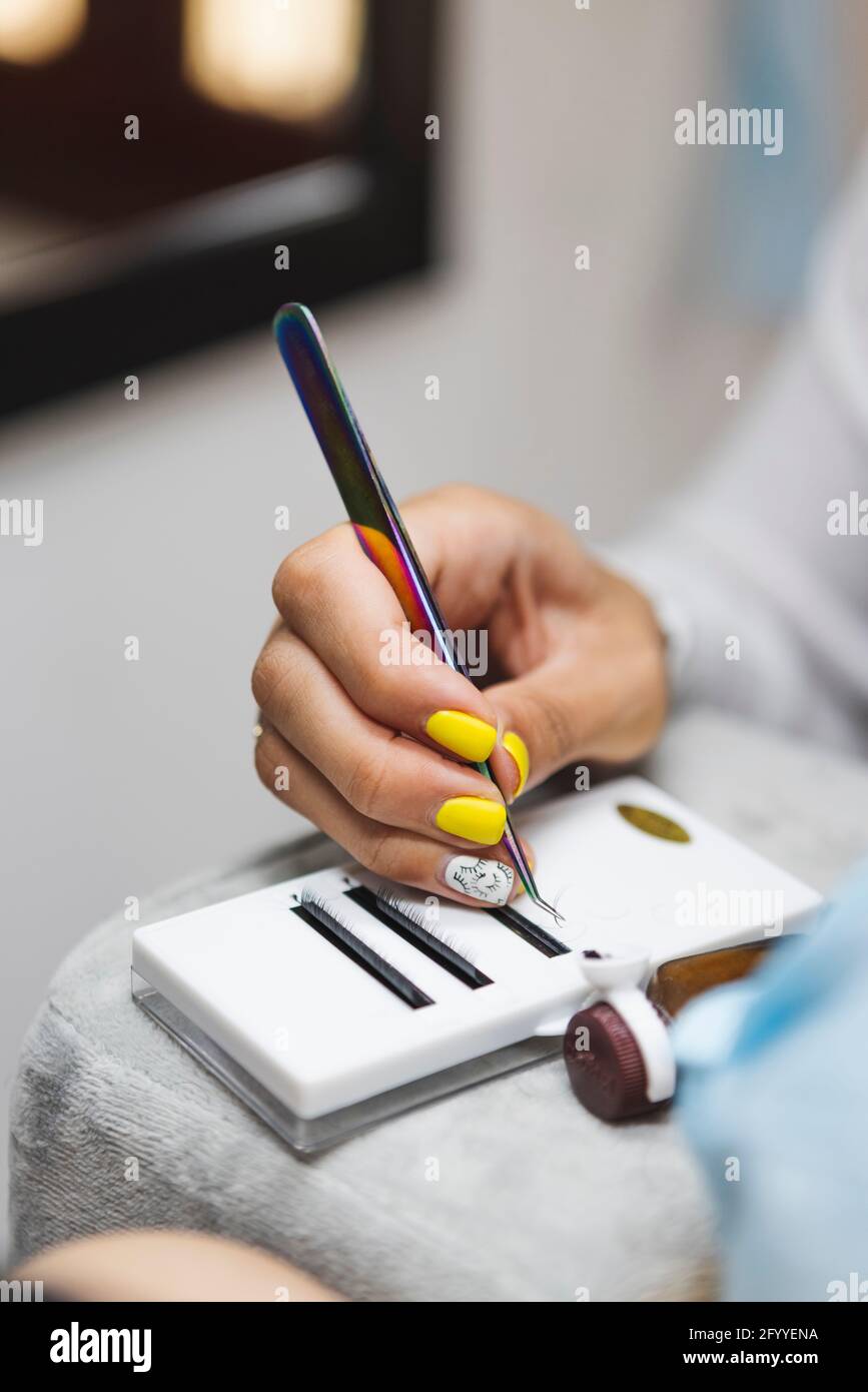 Crop anonyme Beauty-Techniker mit Pinzette unter Wimpern für Verlängerung gegen Frau während der Kosmetologie Verfahren Stockfoto