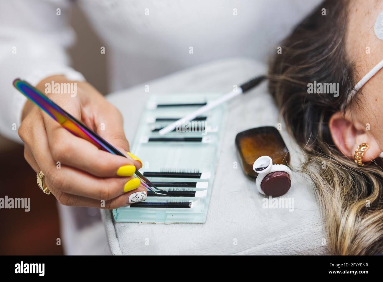 Crop anonyme Beauty-Techniker mit Pinzette unter Wimpern für Verlängerung gegen Frau während der Kosmetologie Verfahren Stockfoto