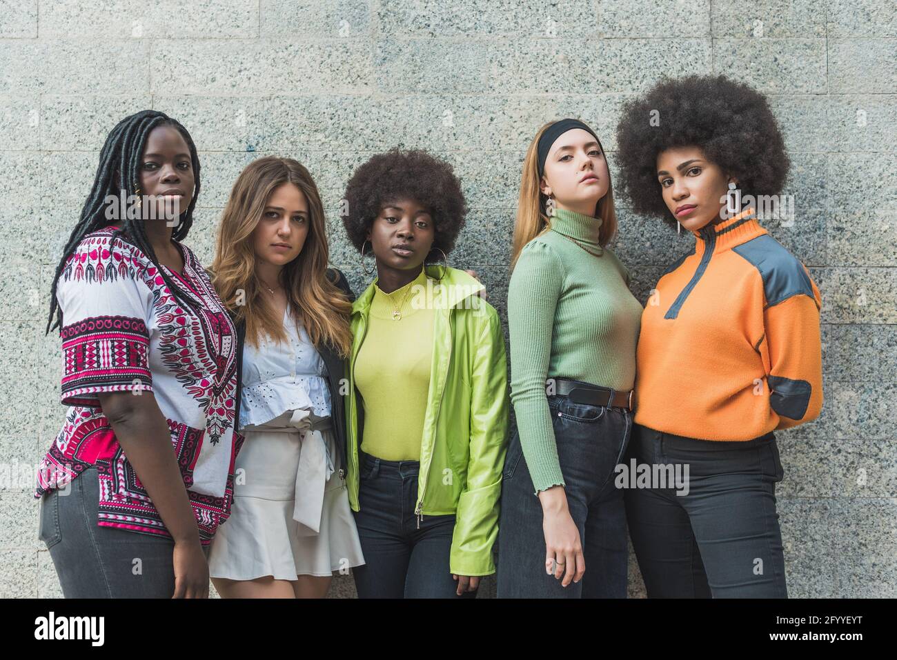 Junge selbstbewusste beste multiethnische Freundinnen, die die Kamera betrachten Auf grauem Hintergrund im Freien Stockfoto
