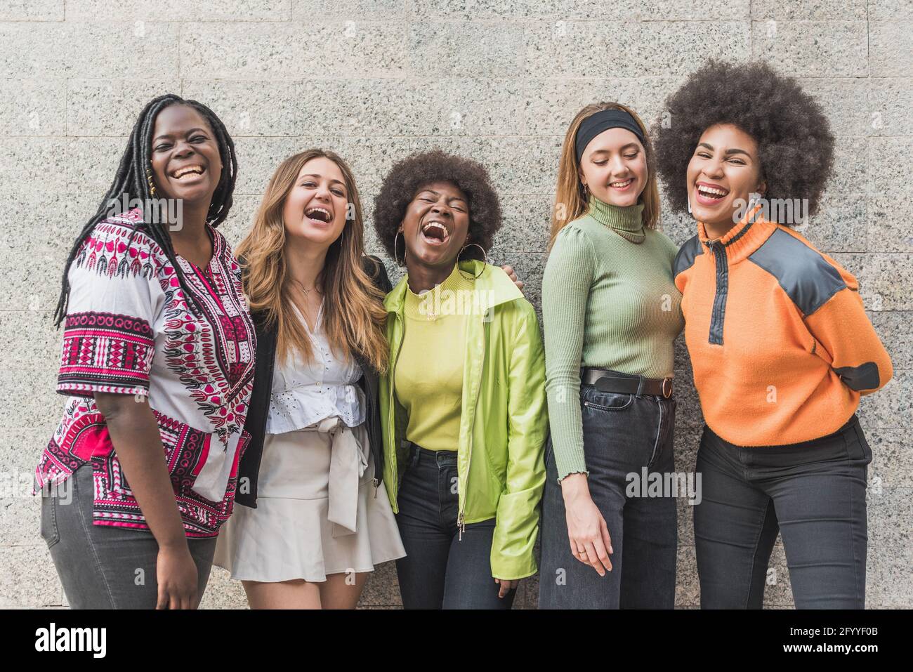 Junge fröhliche selbstbewusste beste multiethnische Freundinnen, die sich anschauen Kamera auf grauem Hintergrund im Freien Stockfoto
