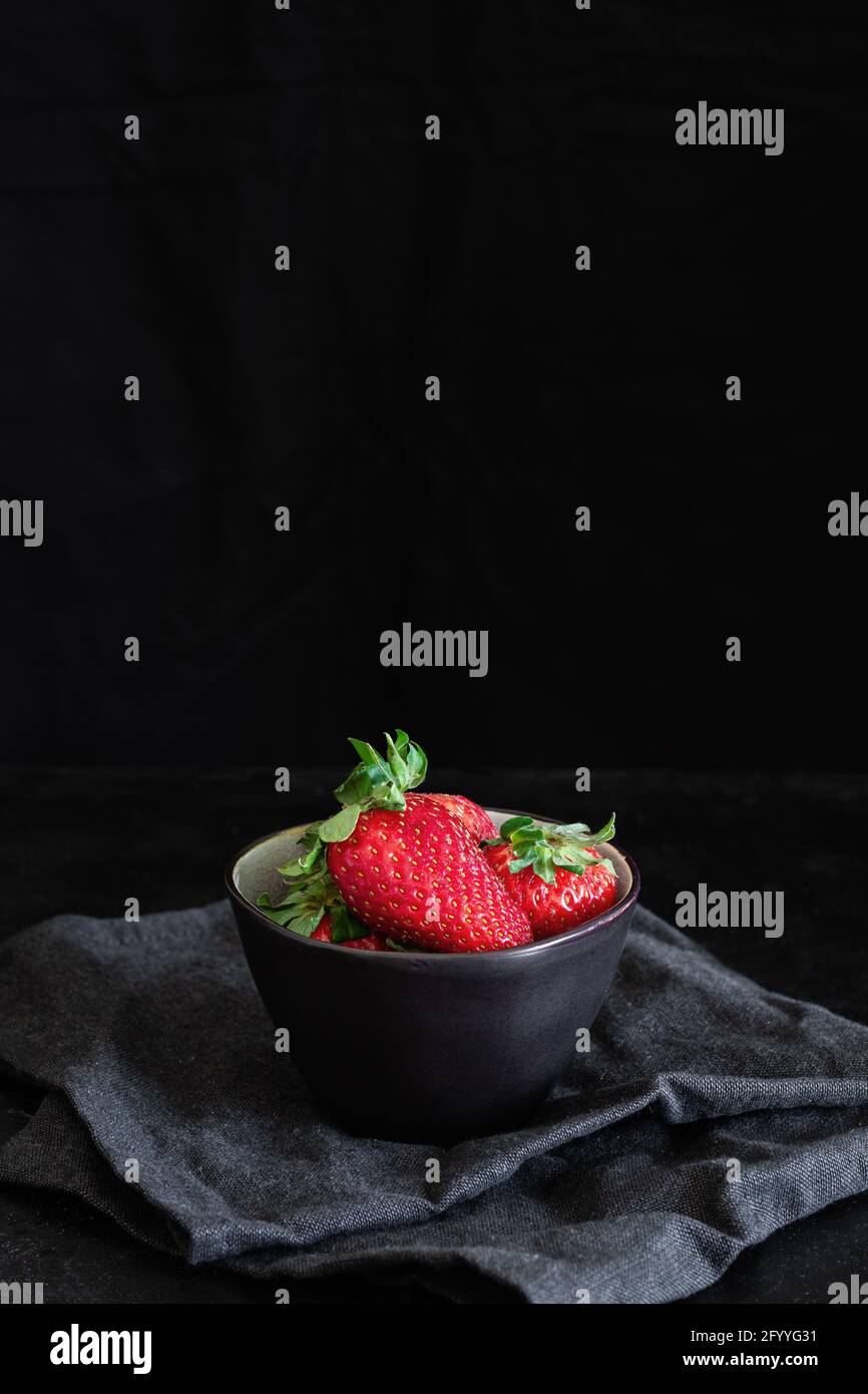 Leckere frische Erdbeeren mit Sepalen in einer runden Schüssel Zerknittertes Textil auf schwarzem Hintergrund Stockfoto
