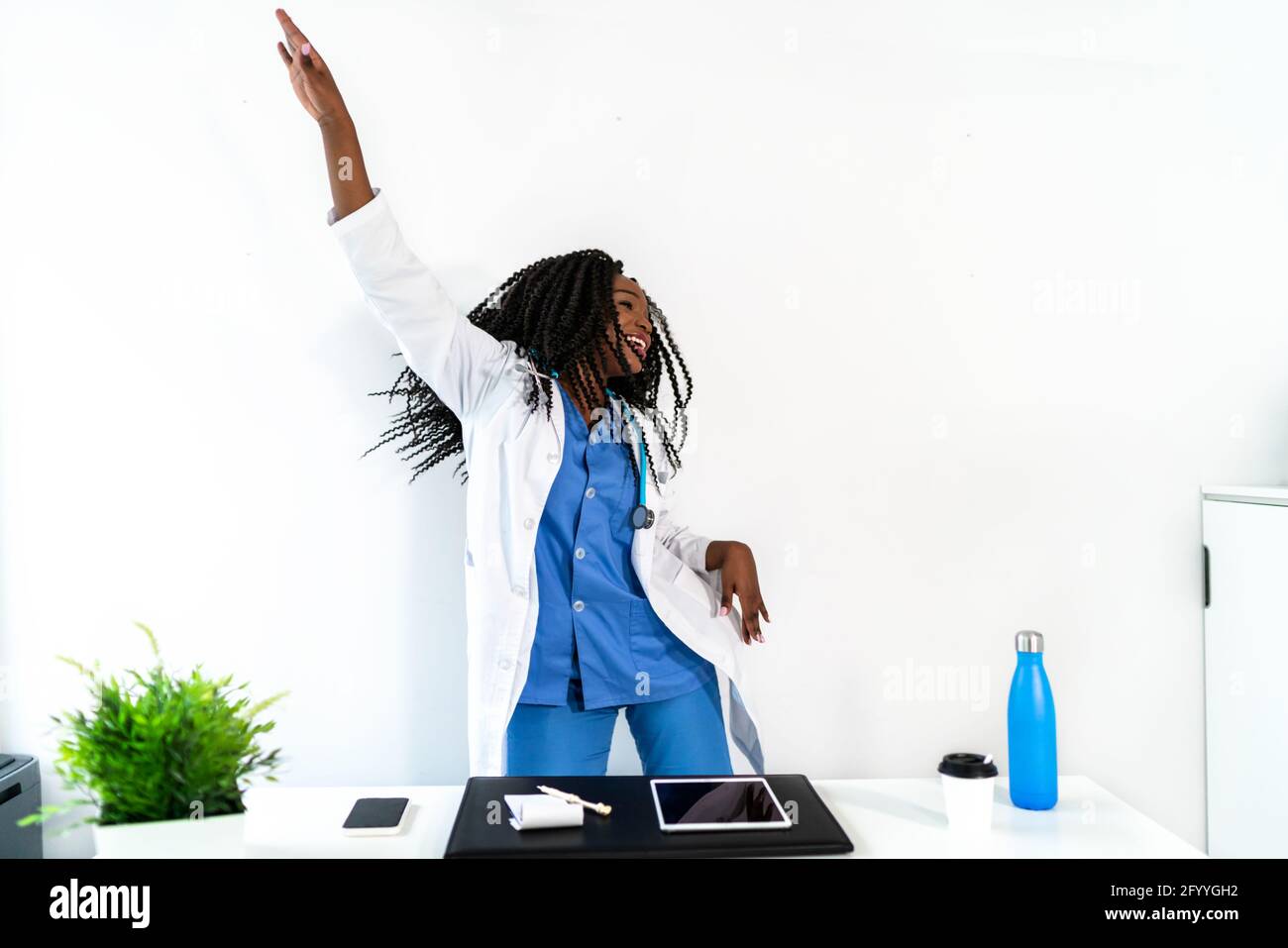 Afroamerikanische Frau in medizinischer Uniform tanzt in der Arztpraxis während der Pause Stockfoto