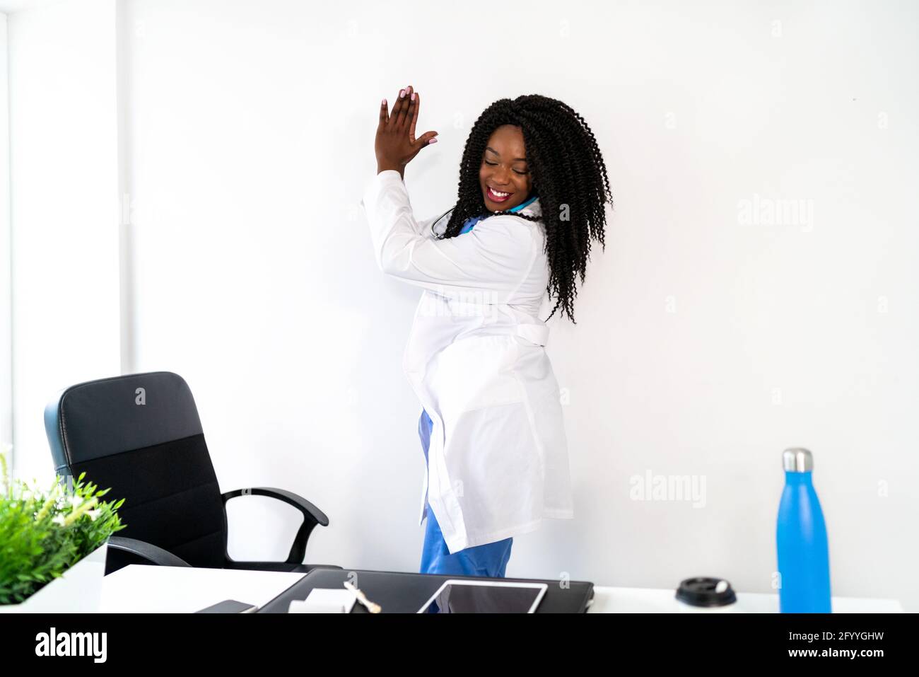 Afroamerikanische Frau in medizinischer Uniform tanzt in der Arztpraxis während der Pause Stockfoto