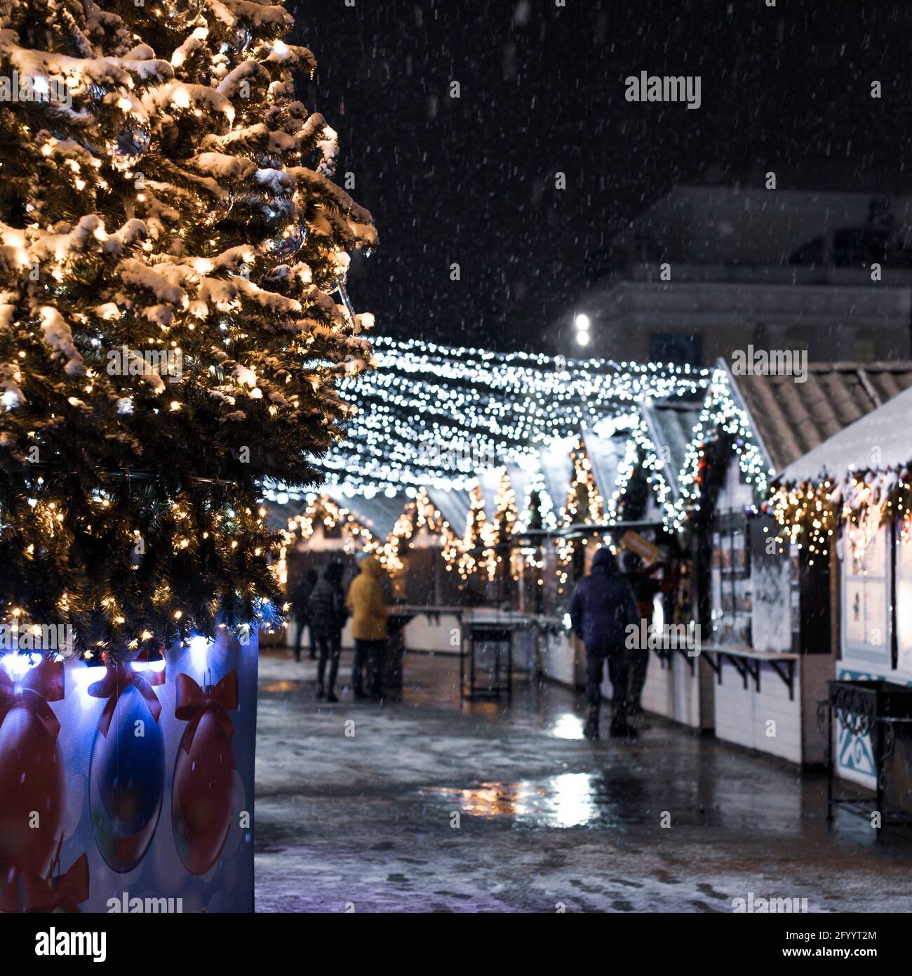 Festliche Weihnachten und der Neujahrsmarkt in der Stadt in der Nacht, fallender  Schnee, Neujahrsbaum und Häuser mit Girlanden Stockfotografie - Alamy