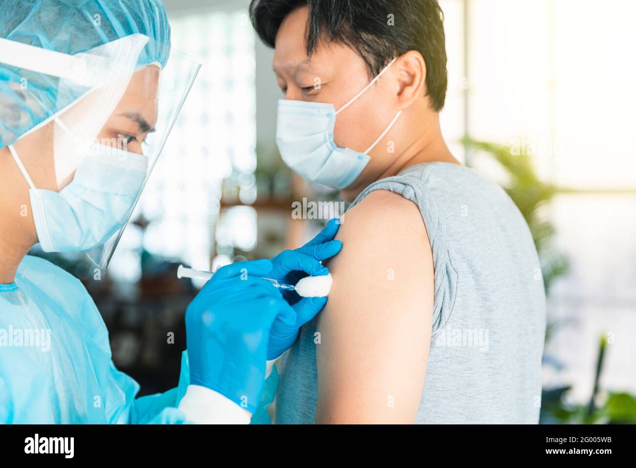 Arzt trägt Gesicht schützende medizinische Maske zum Schutz vor Viren Krankheit mit Spritze, die Impfstoffinjektion an männlichen Patienten macht Stockfoto