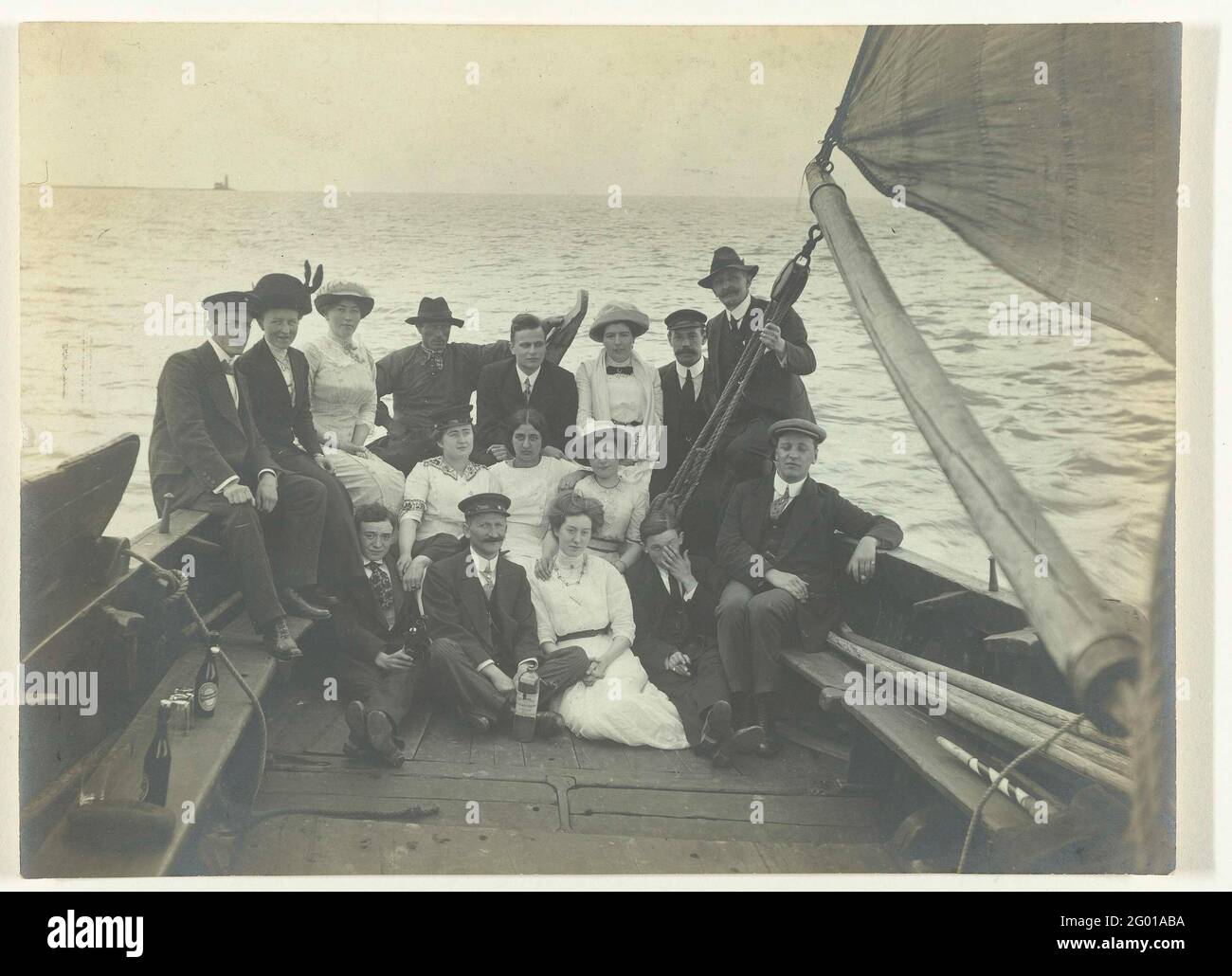 Gruppenportrait einer Gesellschaft auf einem Segelschiff. Sieben Frauen und neun Männer sitzen auf dem Heck eines Segelschiffes. Links auf der Couch Flaschen Bier. Stockfoto