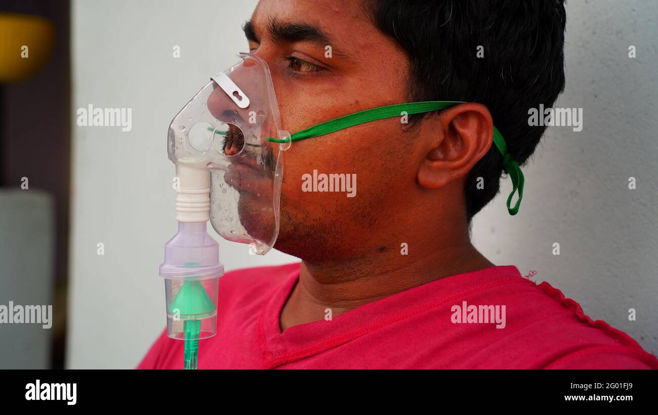 Ein indischer Mann mit Sauerstoffmaske auf dem Gesicht zu Hause während des Lockdown in Rajasthan, Indien. Junge Person sitzt und inhaliert reinen Sauerstoff für Coronavirus. Stockfoto