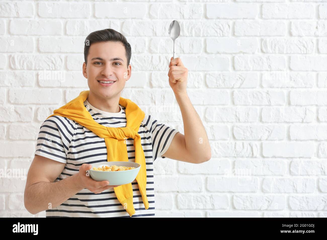 Junger Mann und Schüssel mit Cornflakes auf Backstein Hintergrund Stockfoto