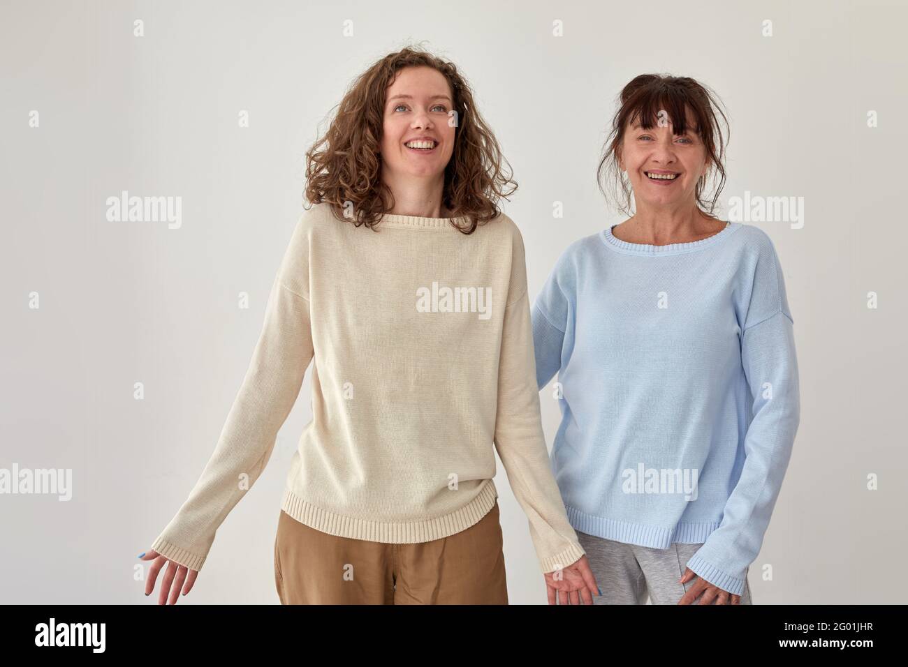Fröhliche Mutter mittleren Alters und Erwachsene Tochter stehen auf grau Hintergrund im Studio und lächelnd Stockfoto