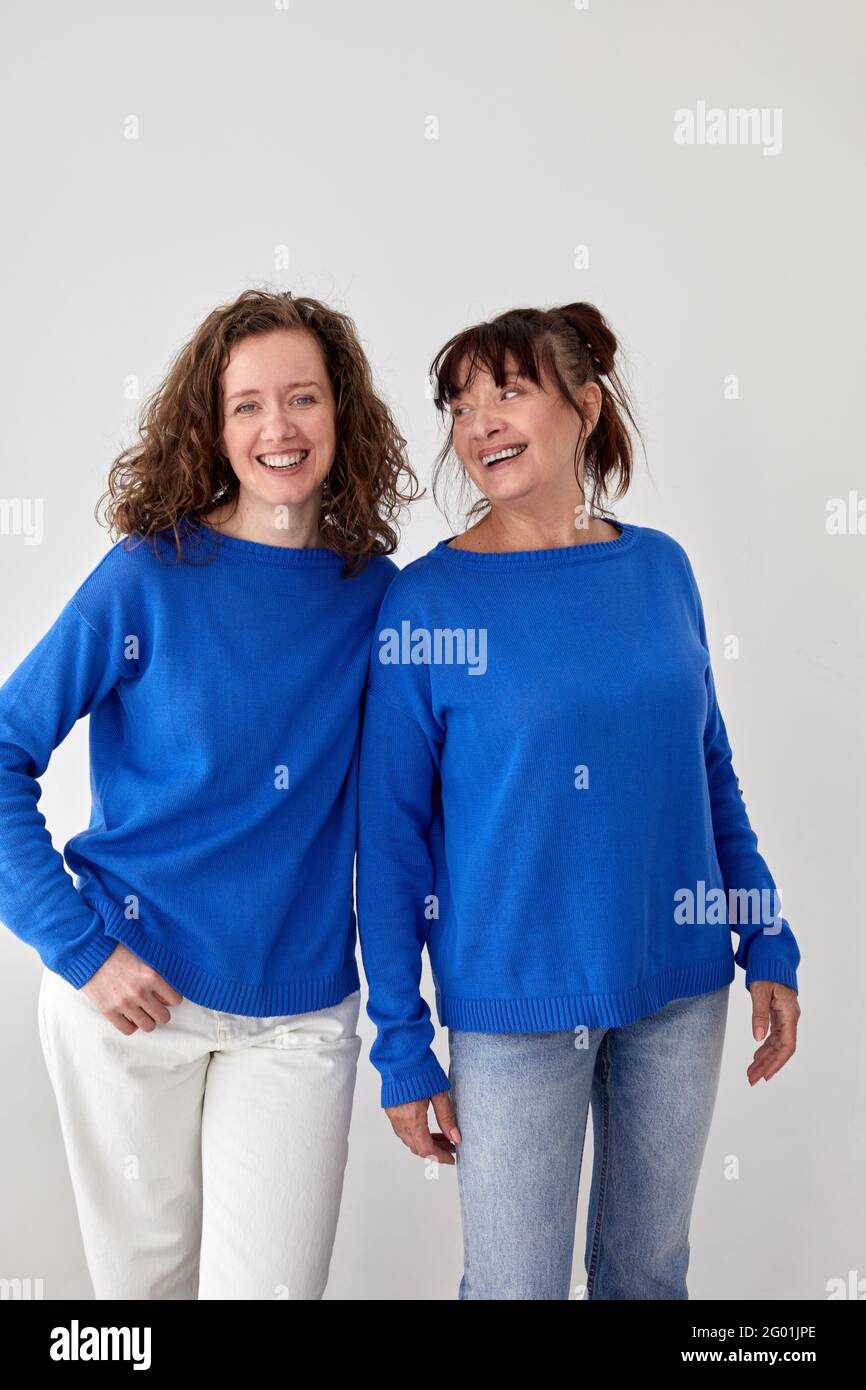 Froh liebende reife Mutter und Erwachsene Tochter tragen ähnlich blau Pullover auf grauem Hintergrund im Studio Stockfoto