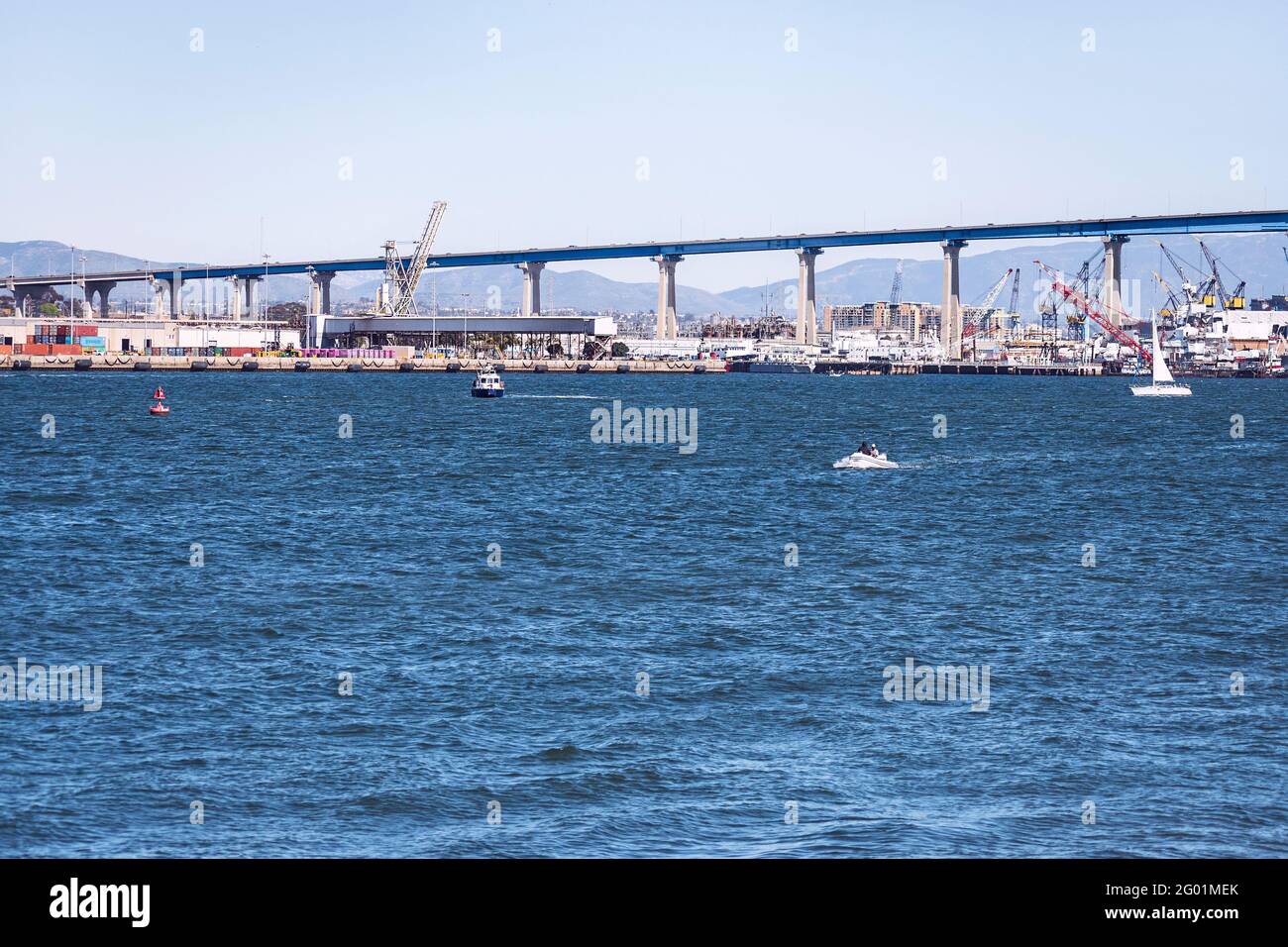 Ein Ausschnitt der Coronado Brücke in San Diego zeigt Werften unter der Brücke mit Bergen im Hintergrund und Boote in der Bucht von San Diego in Th Stockfoto