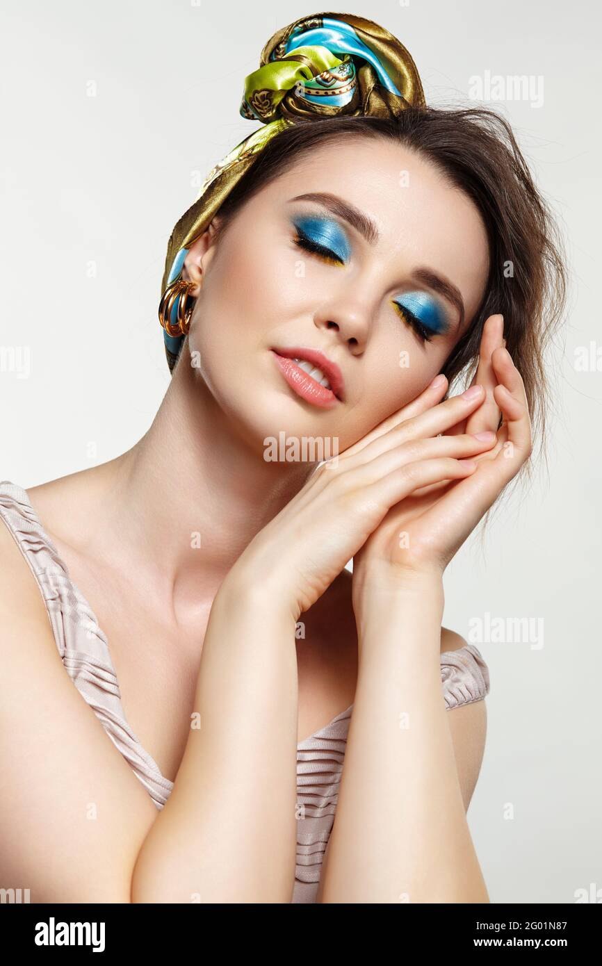 Porträt einer jungen Frau mit geschlossenen Augen Frau posiert im Kopftuch mit der Hand in der Nähe des Gesichts. Make-up mit blauem Lidschatten und gelbem Eyeliner. Stockfoto