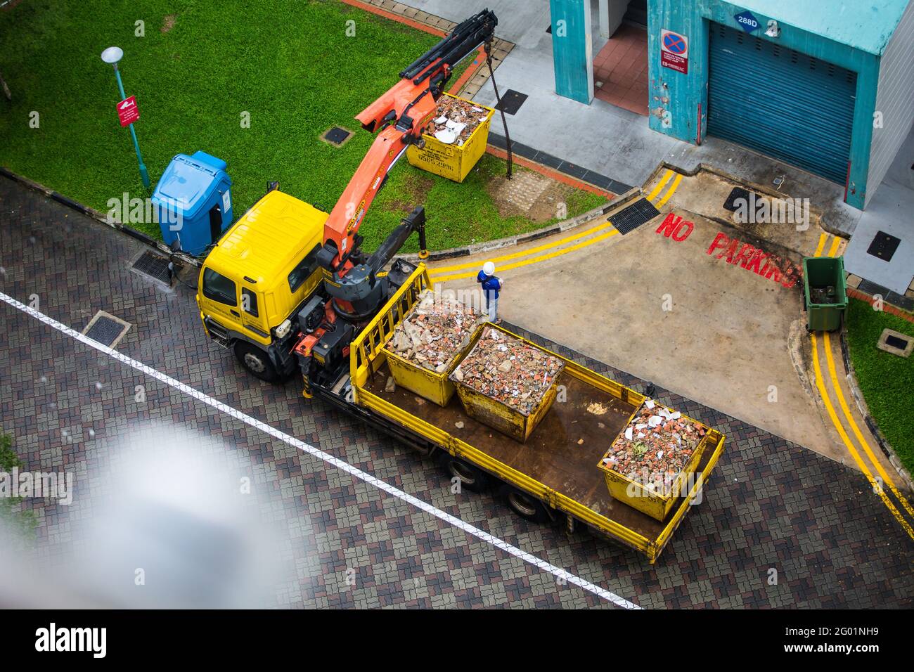 Die Luftaufnahme eines Auslegerlifts vom LKW ist ausgestreckt, um den riesigen, mit Trümmern gefüllten Container anzuheben. Stockfoto