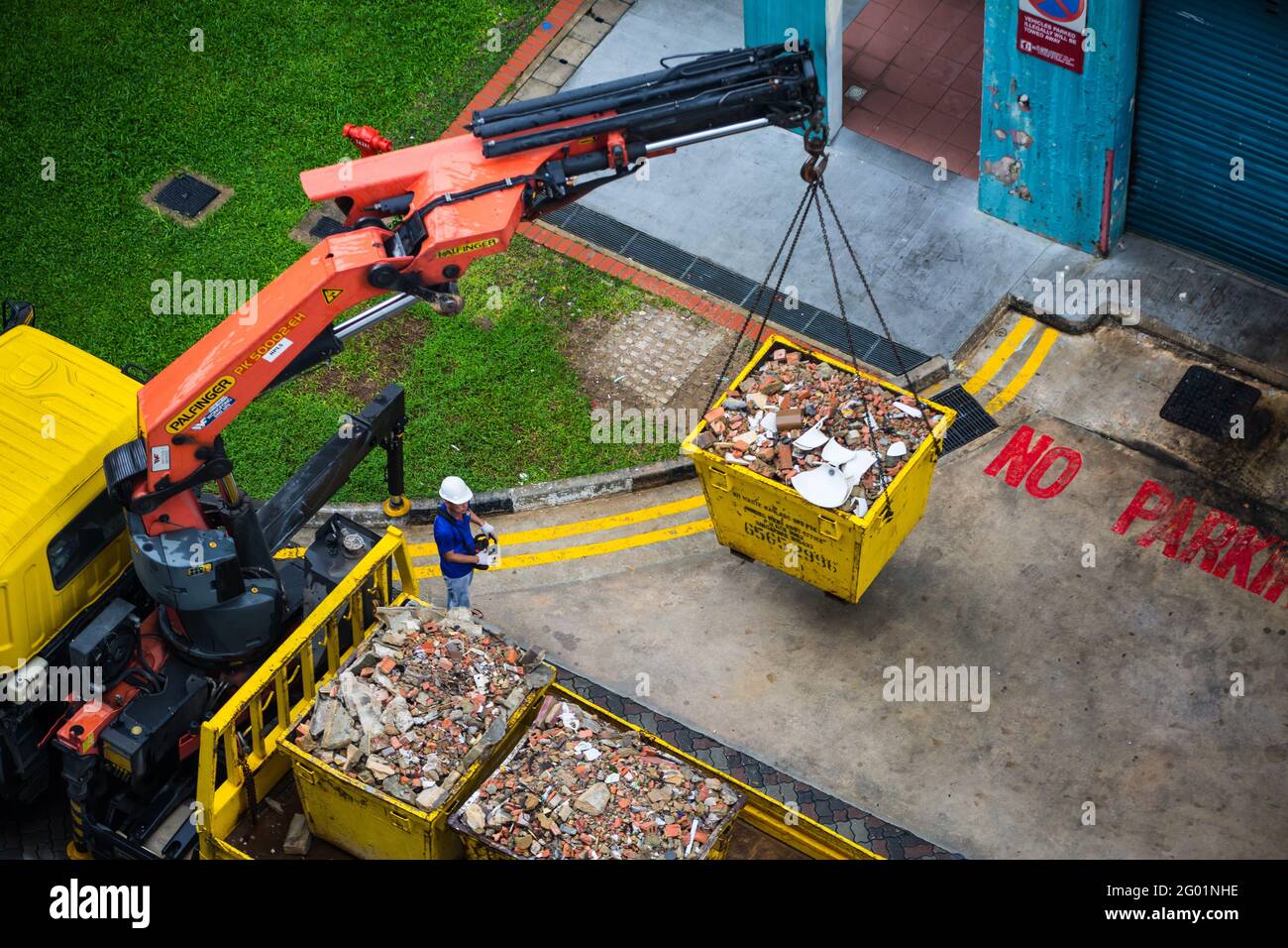 Luftaufnahme eines ein-Mann-Bedieners, der die schweren Industriecontainer hebt und auf die Rückseite des Lastwagens transportiert. Stockfoto