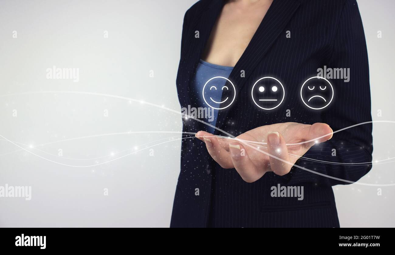 Review, Rating, Zufriedenheitskonzept. Hand halten digitales Hologramm Smiley Face Emoticon auf grauem Hintergrund. Smiley Face Rating für eine Zufriedenheitsumfrage. Stockfoto