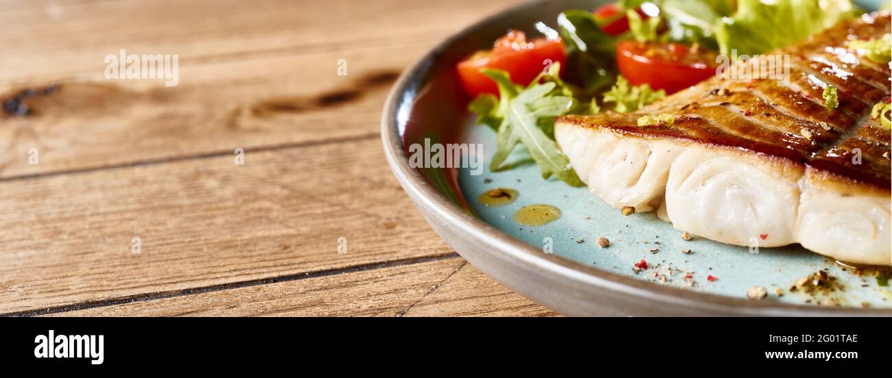 Teller mit appetitlich gebackenem Fischfilet serviert mit frischem Gemüse Salat auf Holztisch Stockfoto