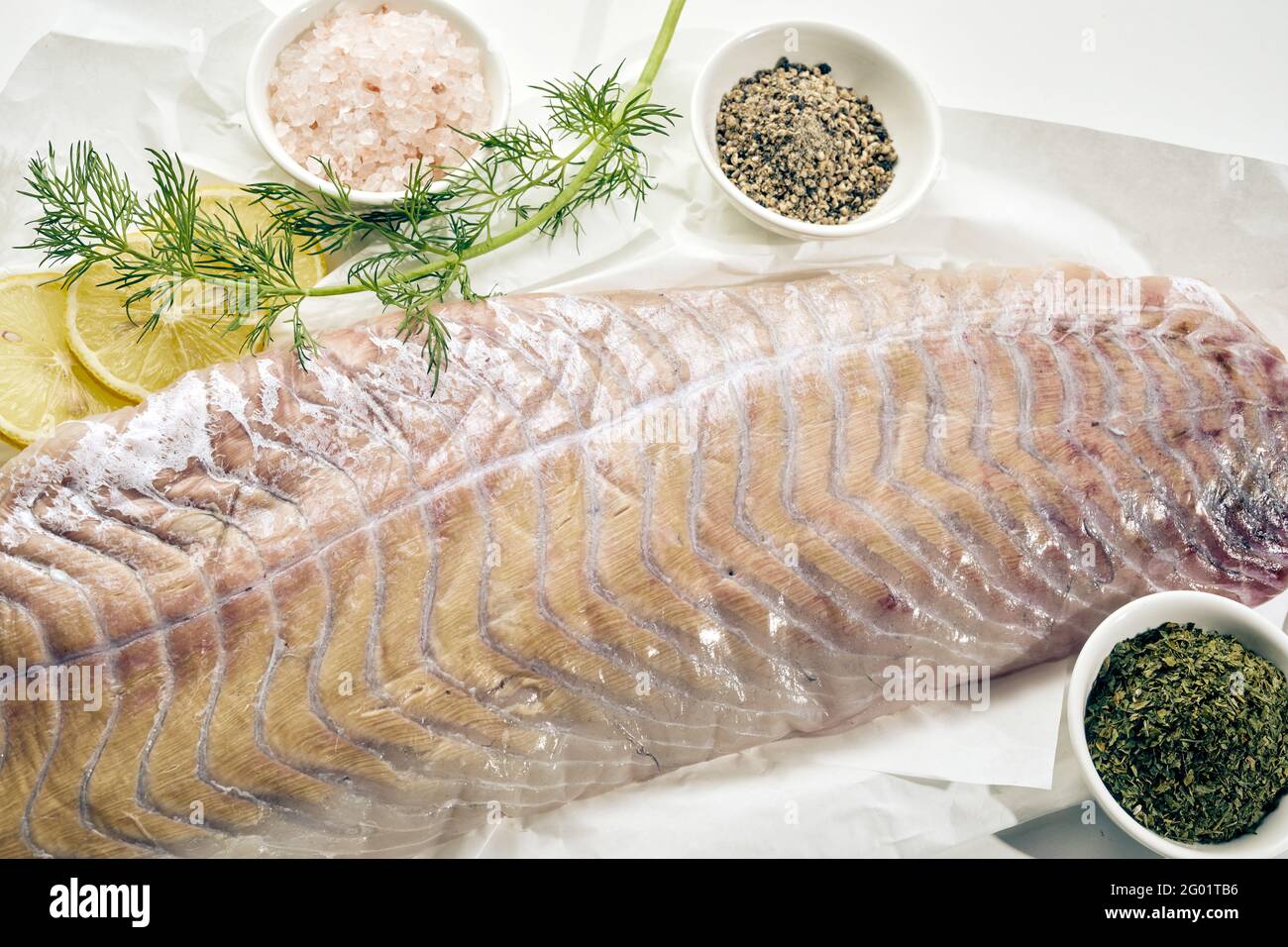 Oben Nahaufnahme des rohen Fischfilets, das zum Kochen vorbereitet ist Mit Dillzweig und Zitronenscheiben mit getrockneten Kräutern und Gewürze und Salz Stockfoto