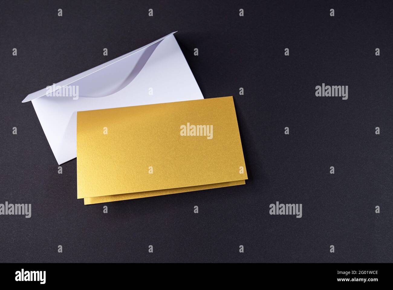 Weißer Umschlag und Einladung als goldenes Quadrat mit leerer Oberfläche auf schwarzem Hintergrund, Mockup, Platz für Text Stockfoto