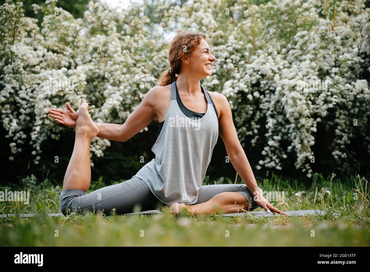 Lächelnde Frau, die Yoga auf grünem Gras macht. Stockfoto