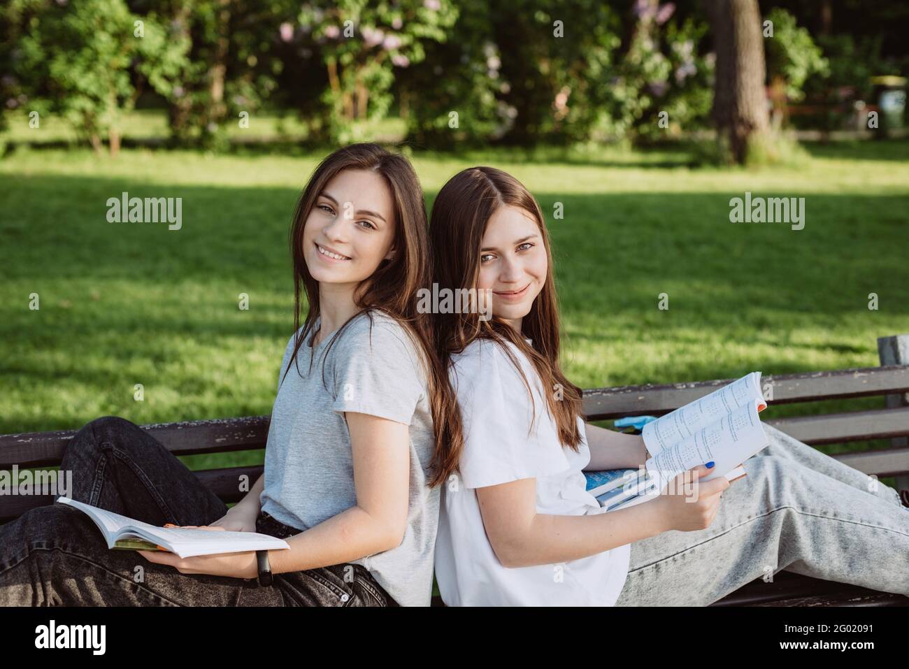 Zwei Studentinnen schauen sich ein offenes Buch auf einer Bank im Park an. Fernunterricht, Vorbereitung auf Prüfungen. Weicher, selektiver Fokus. Stockfoto