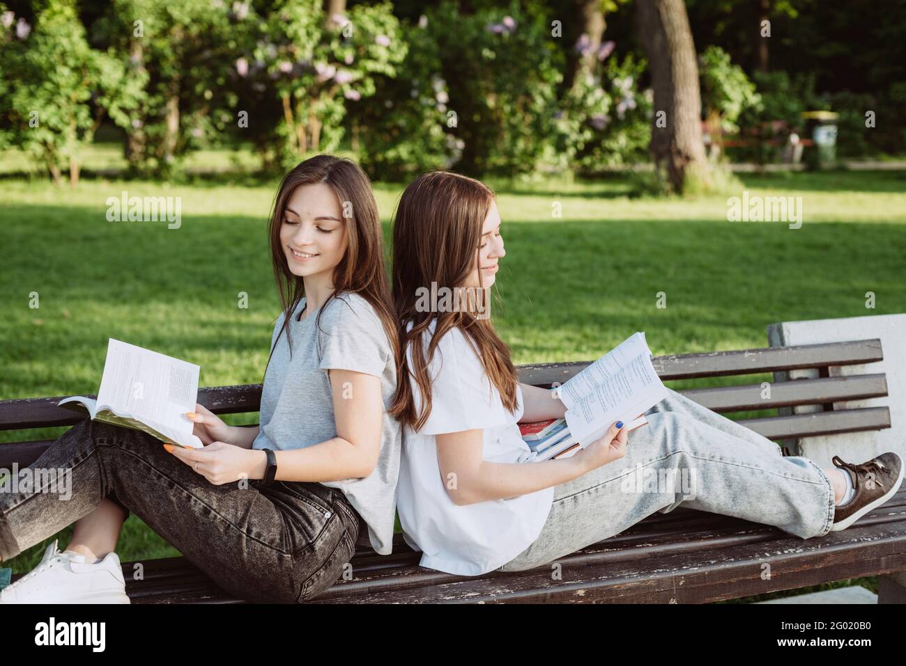 Zwei Studentinnen schauen sich ein offenes Buch auf einer Bank im Park an. Fernunterricht, Vorbereitung auf Prüfungen. Weicher, selektiver Fokus. Stockfoto