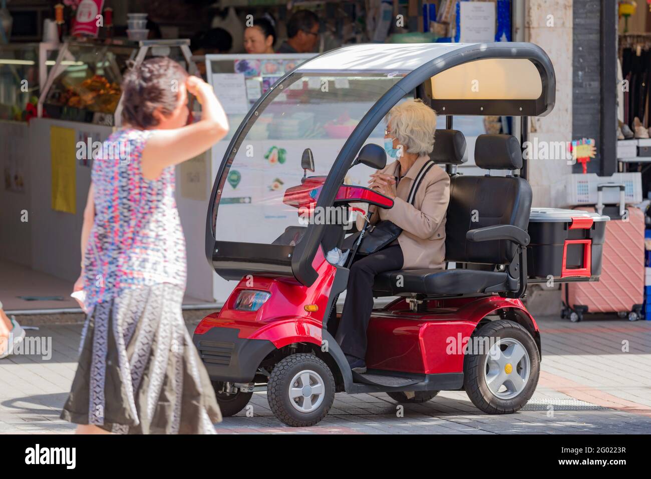 Eine ältere asiatische Frau sitzt in einem überdachten Mobilitätsroller vor einem Geschäft im Vorort Cabramatta New South Wales in Sydney, Australien Stockfoto