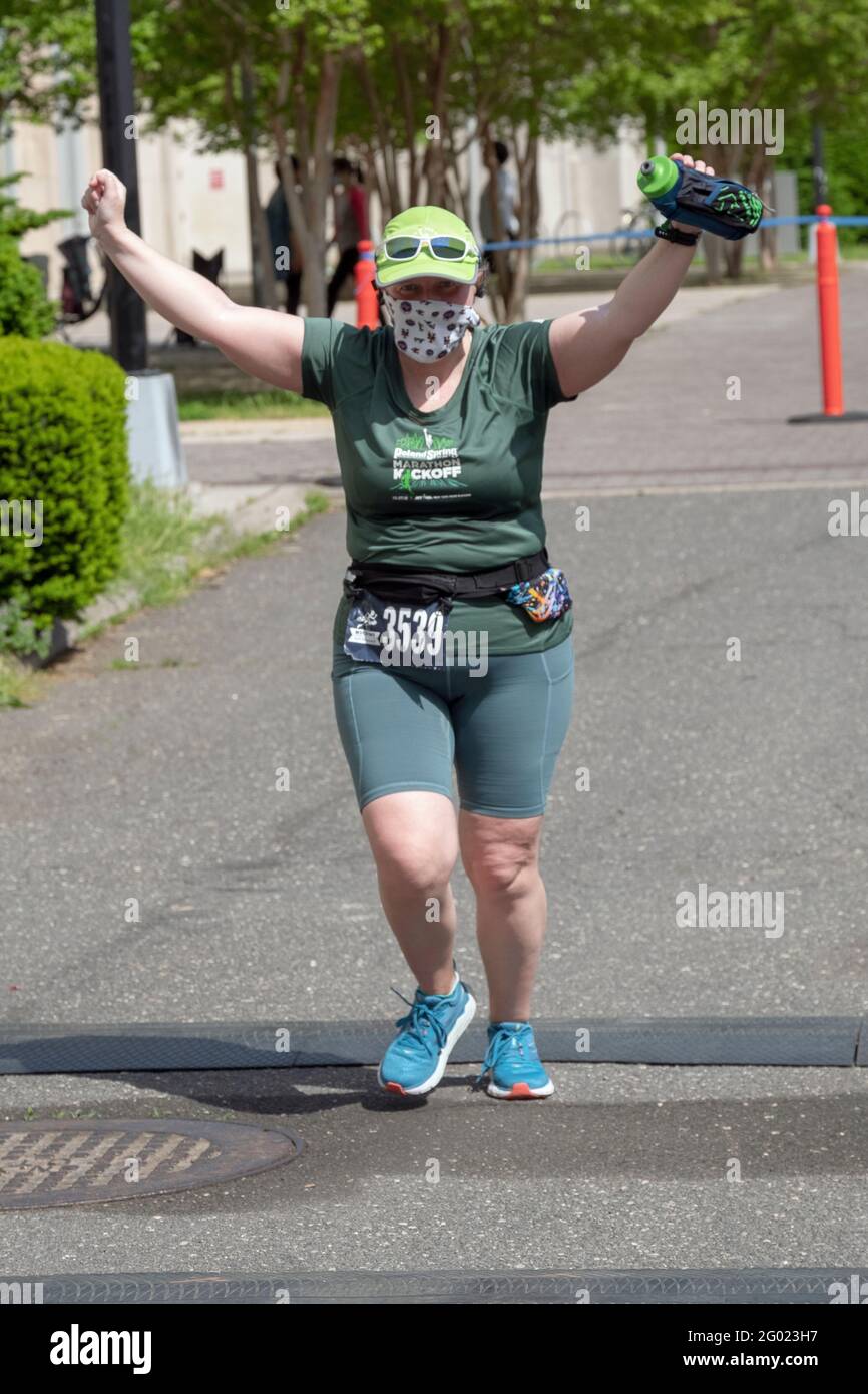 Eine farblich abgestimmte weibliche Finisherin mit Maske nähert sich dem Ende des NYCRuns Queens Halbmarathons in Flushing Meadows Corona. Stockfoto