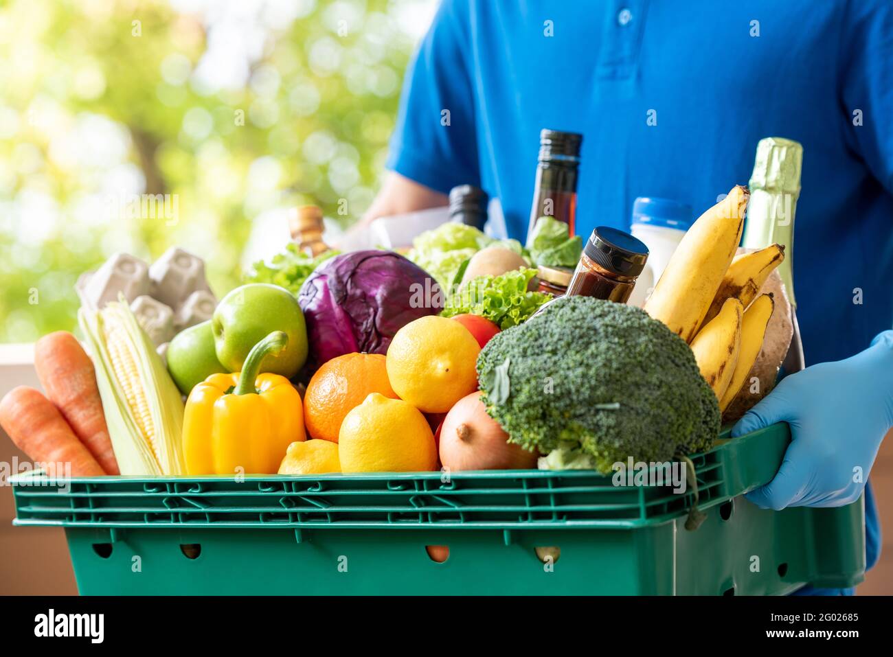 Der Lieferer trägt Handschuhe, die den Lebensmittelkorb halten, um hygienische Lebensmittel zu liefern Service in der Zeit des Pandemiekonzepts Stockfoto