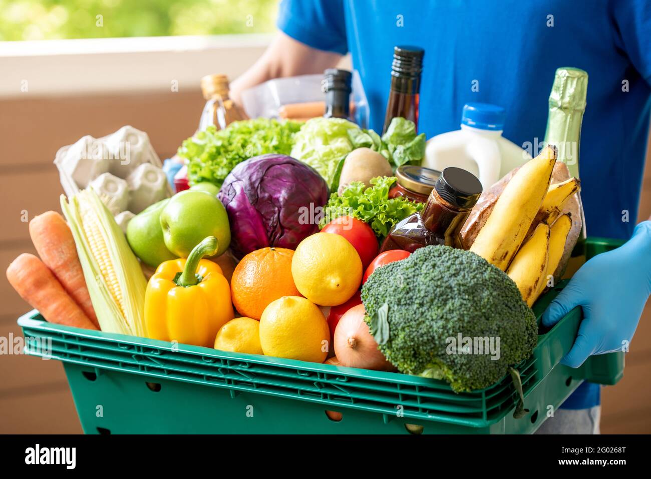 Der Lieferer trägt Handschuhe, die den Lebensmittelkorb halten, um hygienische Lebensmittel zu liefern Service in der Zeit des Pandemiekonzepts Stockfoto