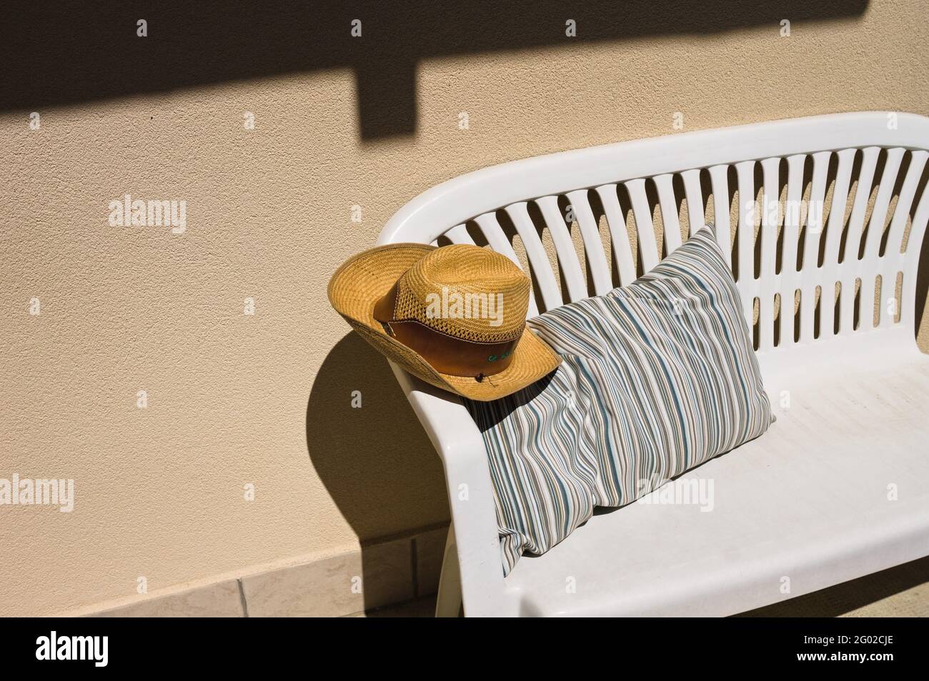 Ein Cowboy-Weidenhut auf einer weißen Bank mit einem gestreiften Vintage-Kissen im Garten (Marken, Italien, Europa) Stockfoto