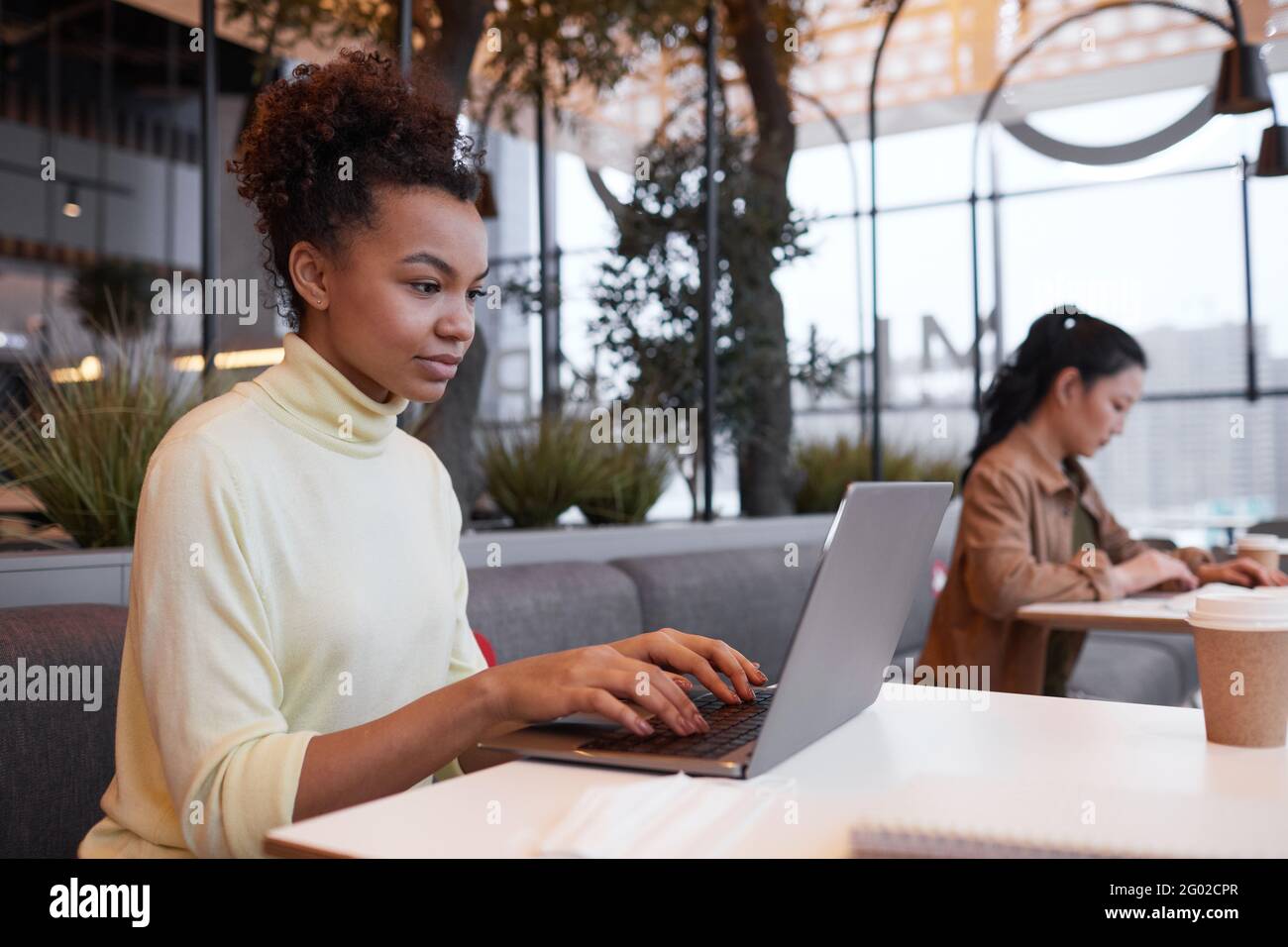 Porträt einer jungen afroamerikanischen Frau, die einen Laptop benutzt, während sie am Tisch im Café arbeitet, Platz zum Kopieren Stockfoto