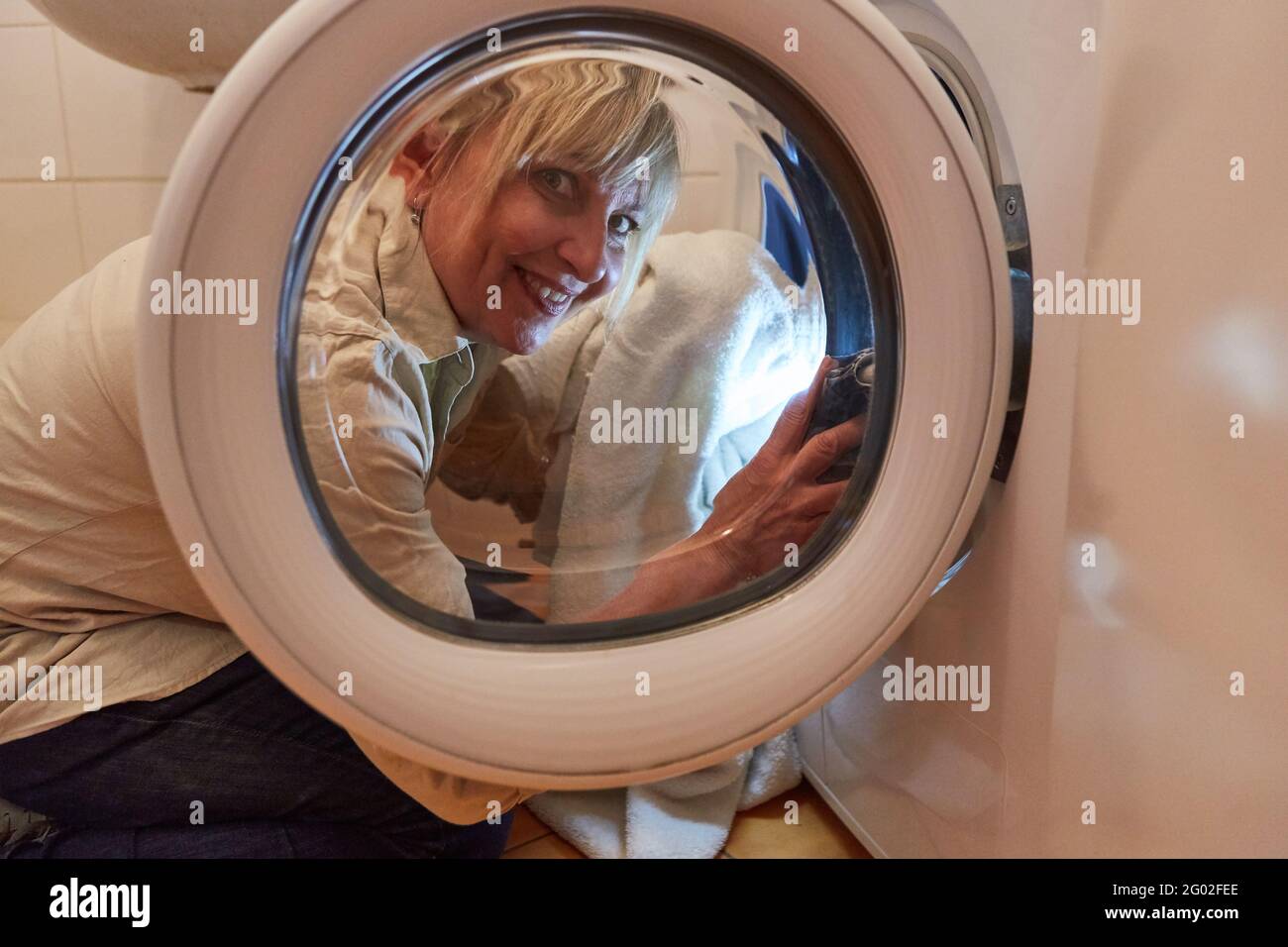 Lächelnde Frau als Hausfrau füllt den Wäschetrockner oder Waschmaschine Stockfoto