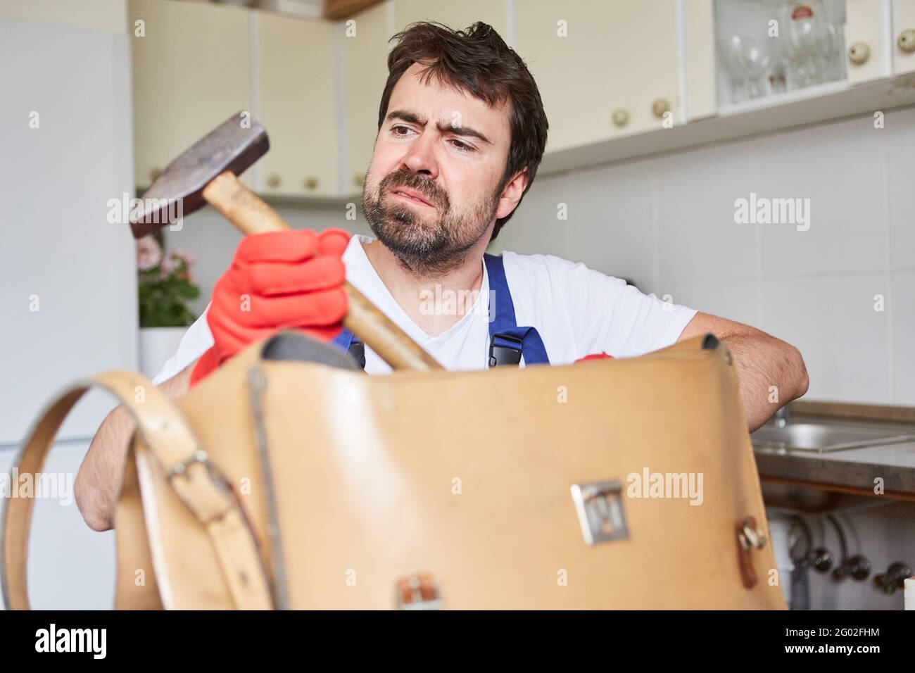 Heimwerker oder Handwerker blicken skeptisch auf einen Hammer in seinem Werkzeugtasche Stockfoto