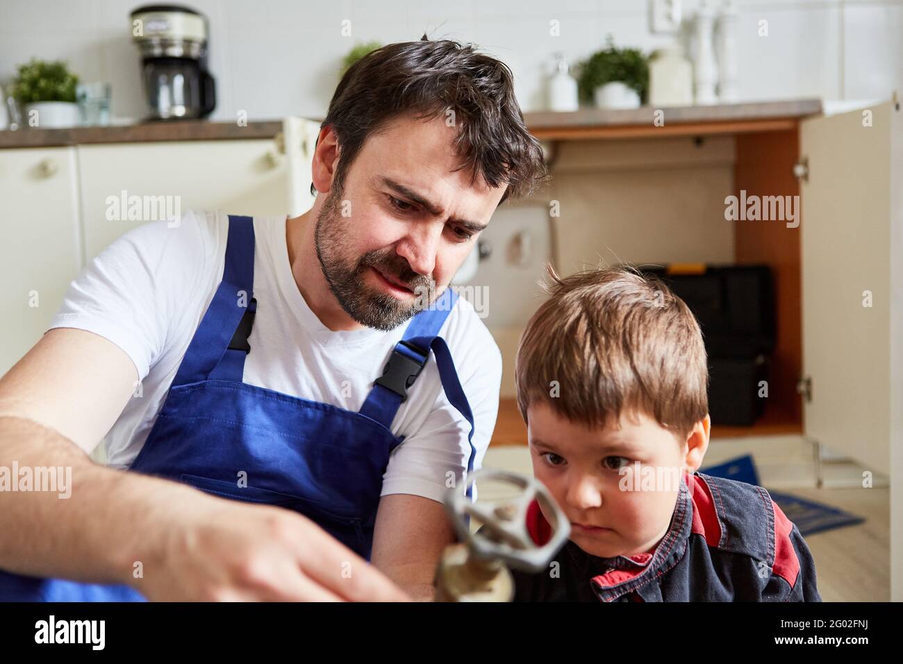 Kind und Vater schauen sich zur Reparatur ein Absperrventil an Das kaputte Waschbecken in der Küche Stockfoto