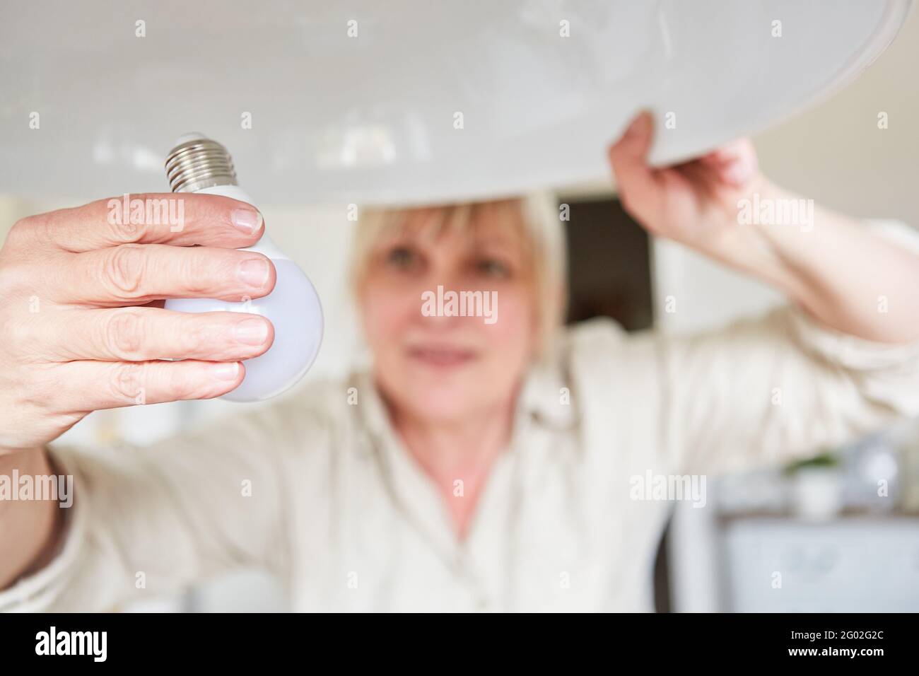 Frau tauscht alte Glühbirne gegen Energiesparlampe aus, um Nachhaltigkeit zu gewährleisten Stockfoto