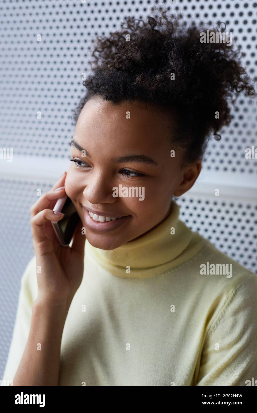 Vertikales Nahaufnahme-Porträt einer jungen afroamerikanischen Frau, die durch spricht Smartphone und fröhlich lächelnd Stockfoto