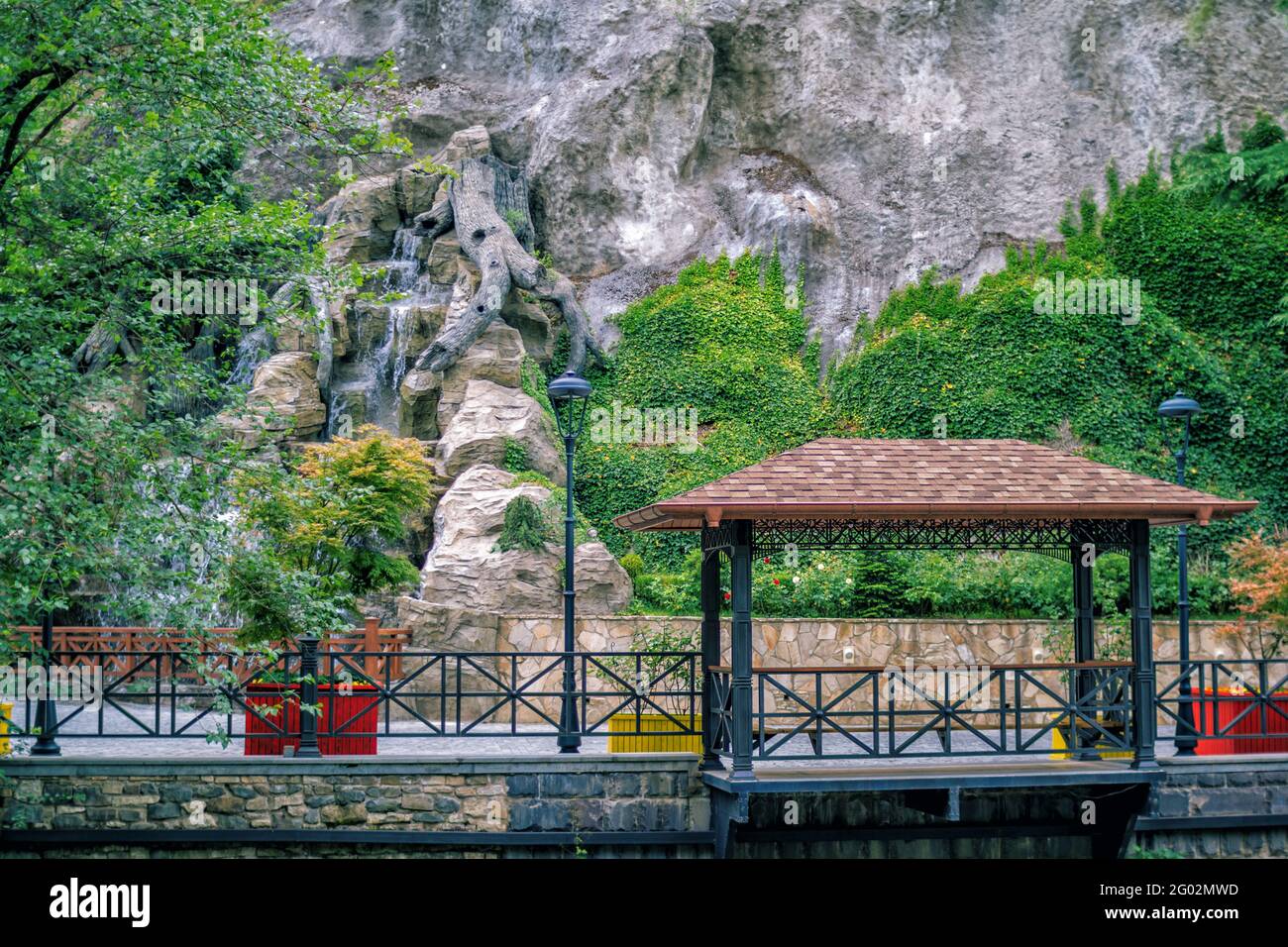 Sommerlandschaft - schöner Park - grün bewachsener Efeu bedeckt Bergsteinoberfläche, künstlichen Wasserfall und Gartenlaube. Stockfoto