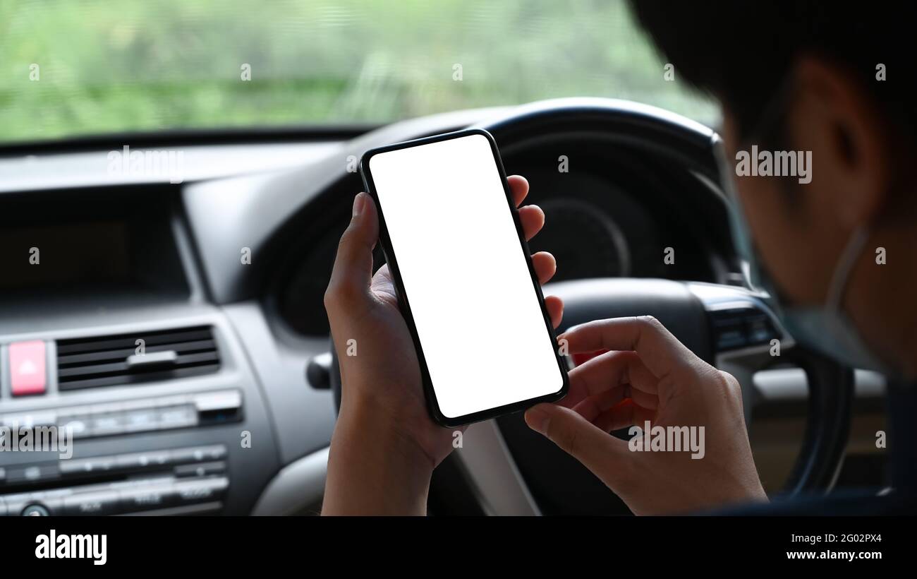 Nahaufnahme eines jungen asiatischen Mannes mit Schutzmaske und Mobiltelefon, während er in seinem Auto sitzt. Stockfoto