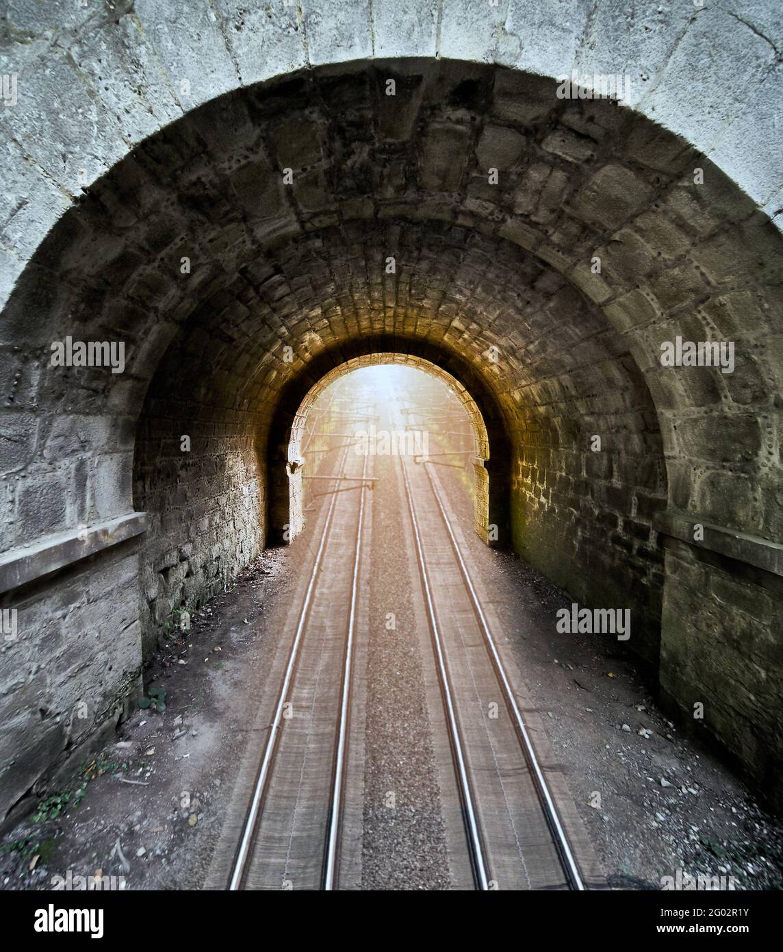 Dunkler Durchgang aus grob behauenen Steinen mit einem runden Bogen, durch den zwei Eisenbahnlinien verlaufen, zusammengesetztes surreales Bild Stockfoto