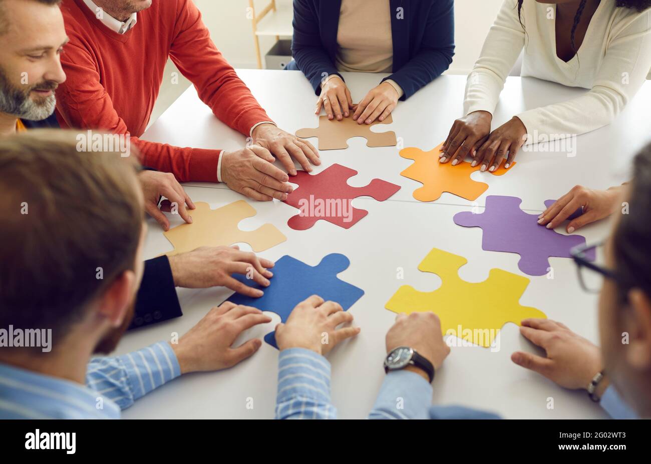 Verschiedene multiethnische Gruppen arbeiten zusammen, um Puzzleteile zusammenzubauen Stockfoto
